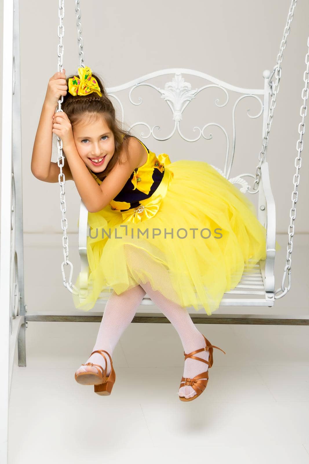 Beautiful little girl swinging in the studio on a swing. Concept of a happy childhood, family well-being.