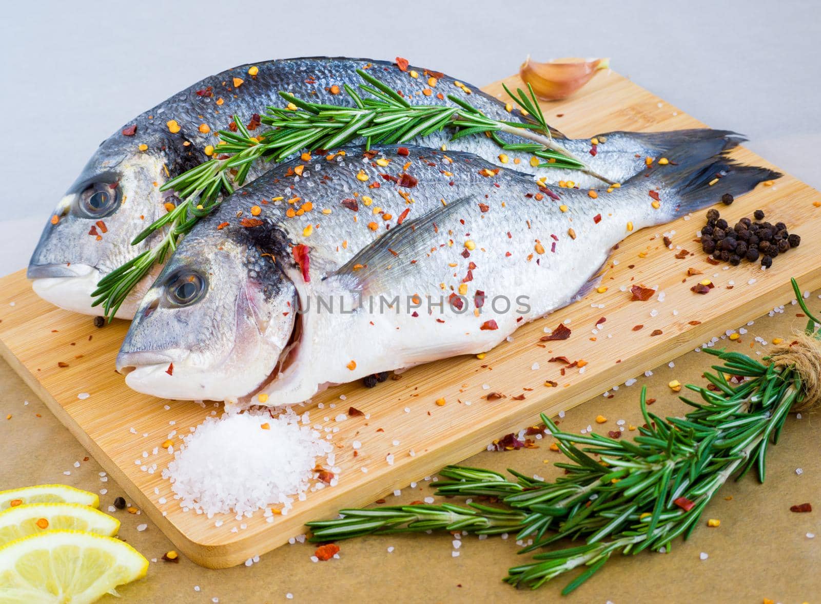 Mediterranean seafood concept. Raw dorado fish with lemon, spices and rosemary on wooden board. Fresh organic sea bream or dorada fish.