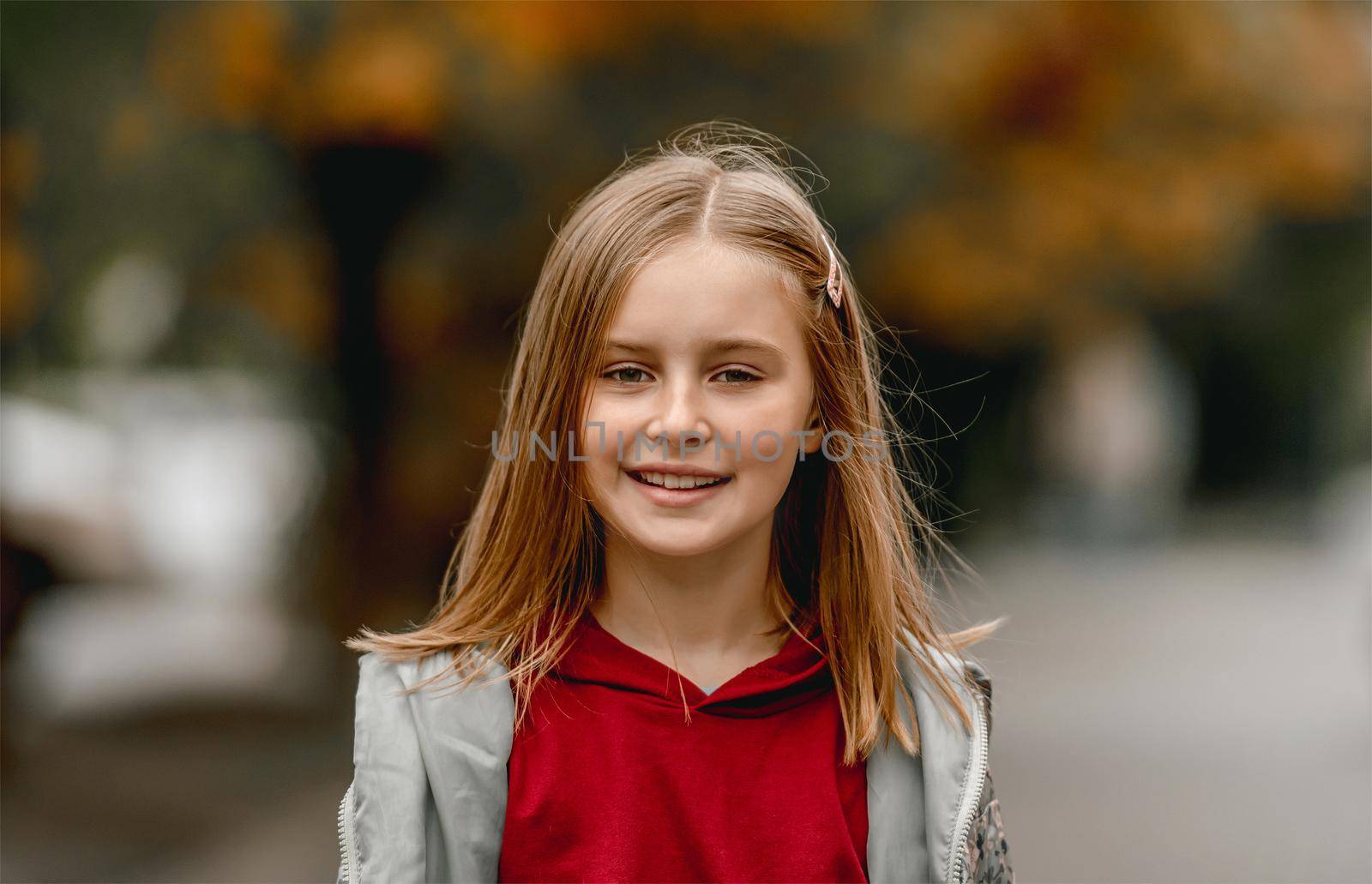 Preteen girl autumn portrait. Pretty kid smiling and looking at camera outdoors