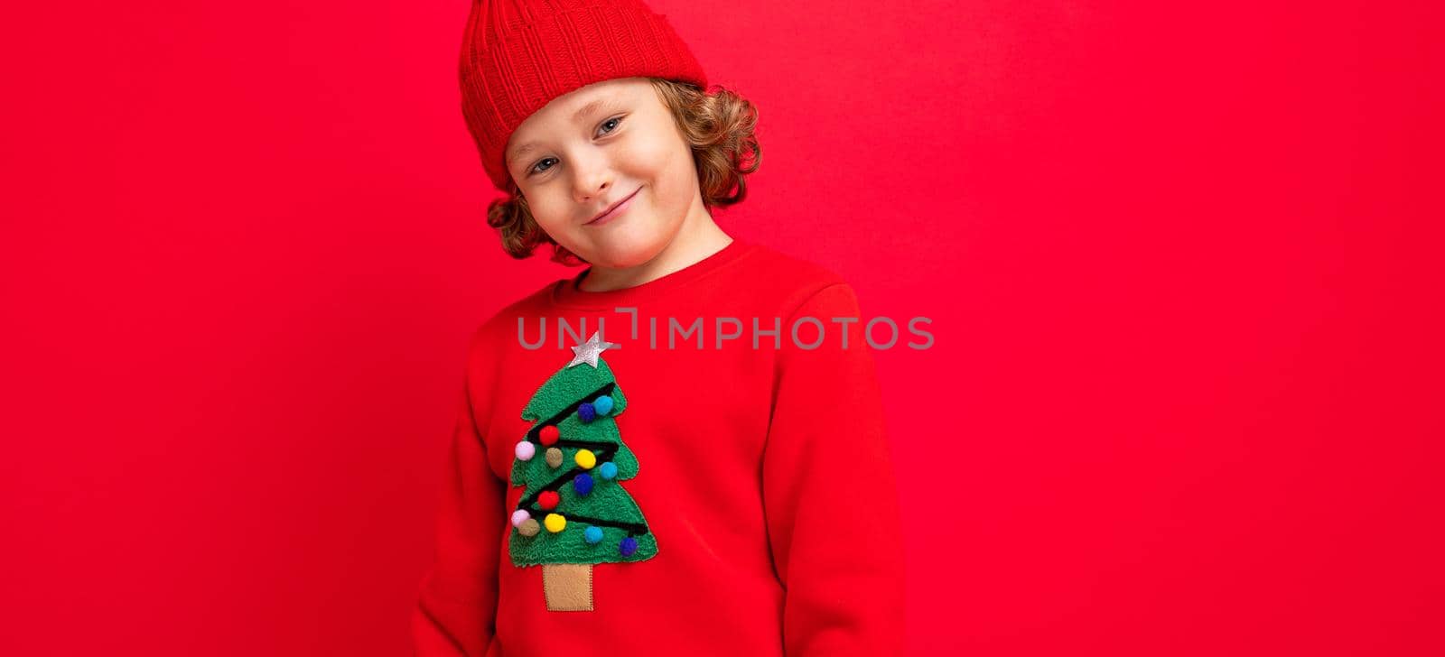 cool boy with curls on a red background in a sweater with a christmas tree.