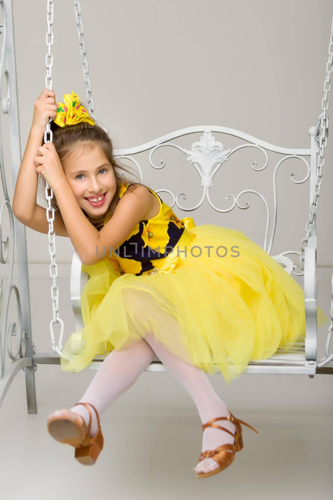 Beautiful little girl swinging in the studio on a swing. Concept of a happy childhood, family well-being.