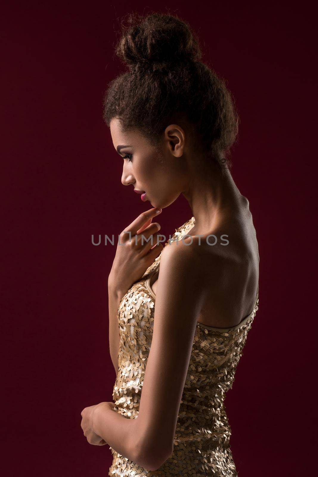 Fashion young African woman with makeup, in sexy gold dress. Model on a red background in the studio. A woman is half a turn