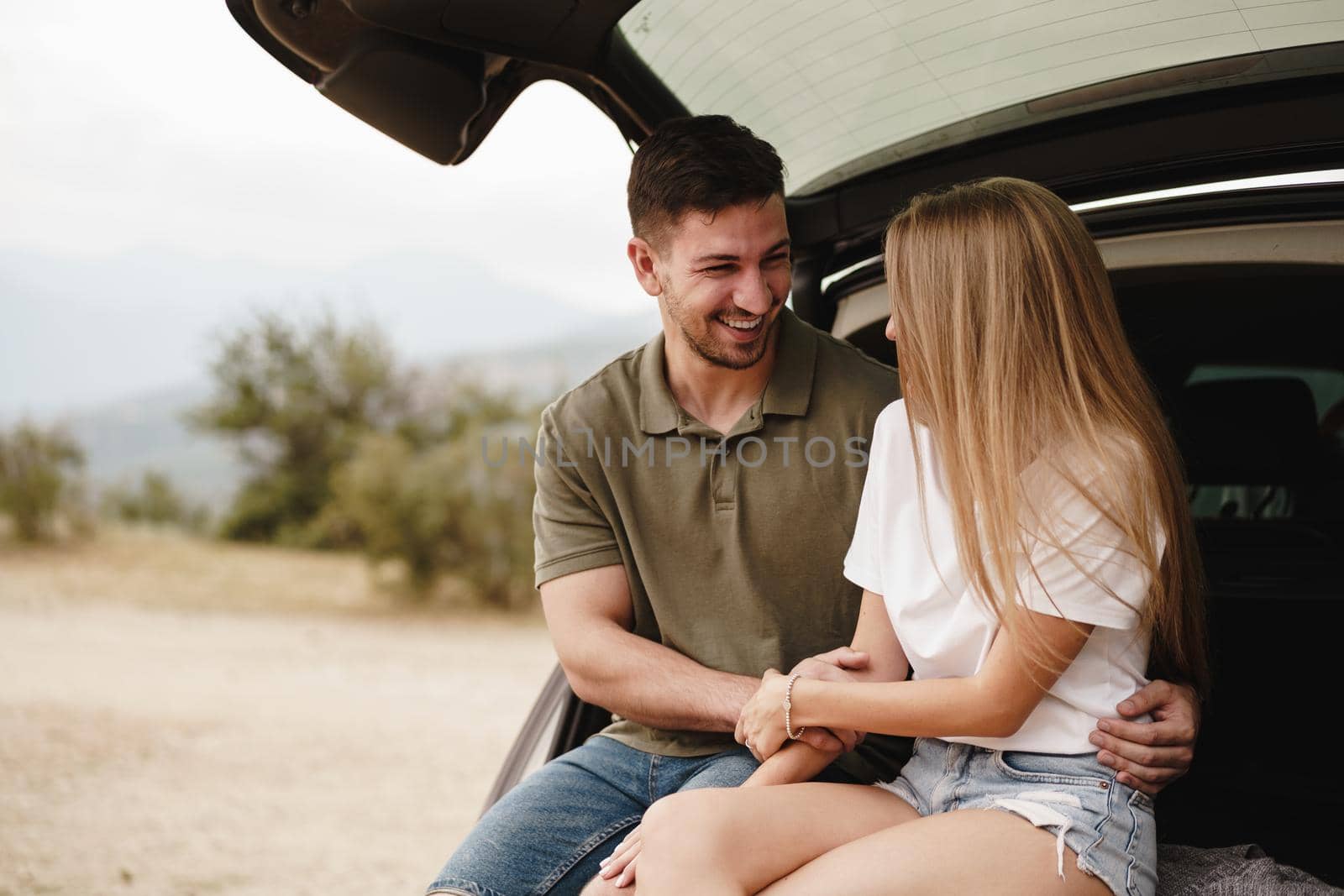 Young happy couple on a road trip sitting in car trunk outdoor