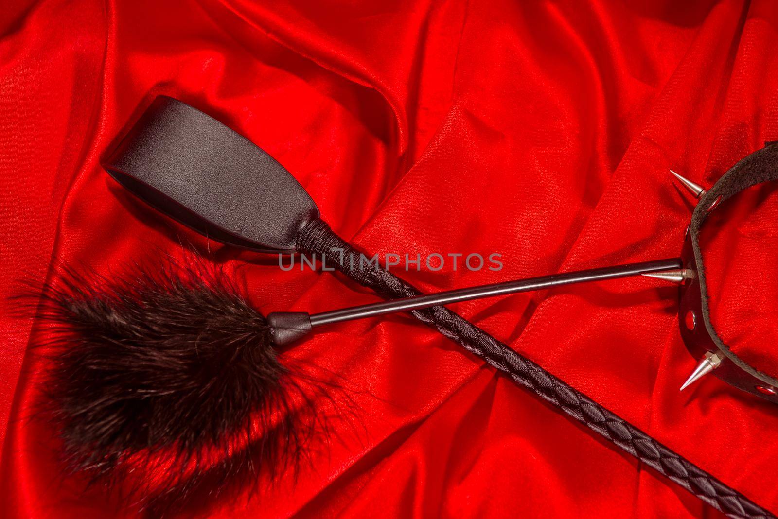 Bondage, kinky adult sex games, kink and BDSM lifestyle concept with a whip, feather stick, collar on red silk with copy space