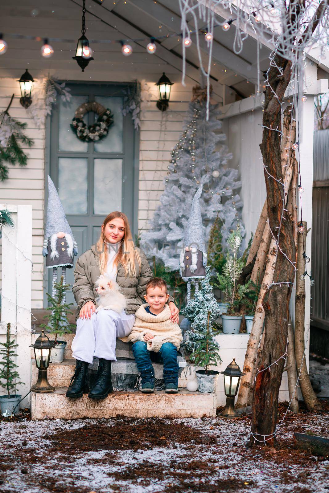 Happy little kids with white little puppy sitting on the porch of the Christmas decorated house, snowing outdoor. Happy New Year and Merry Christmas. Magic winter