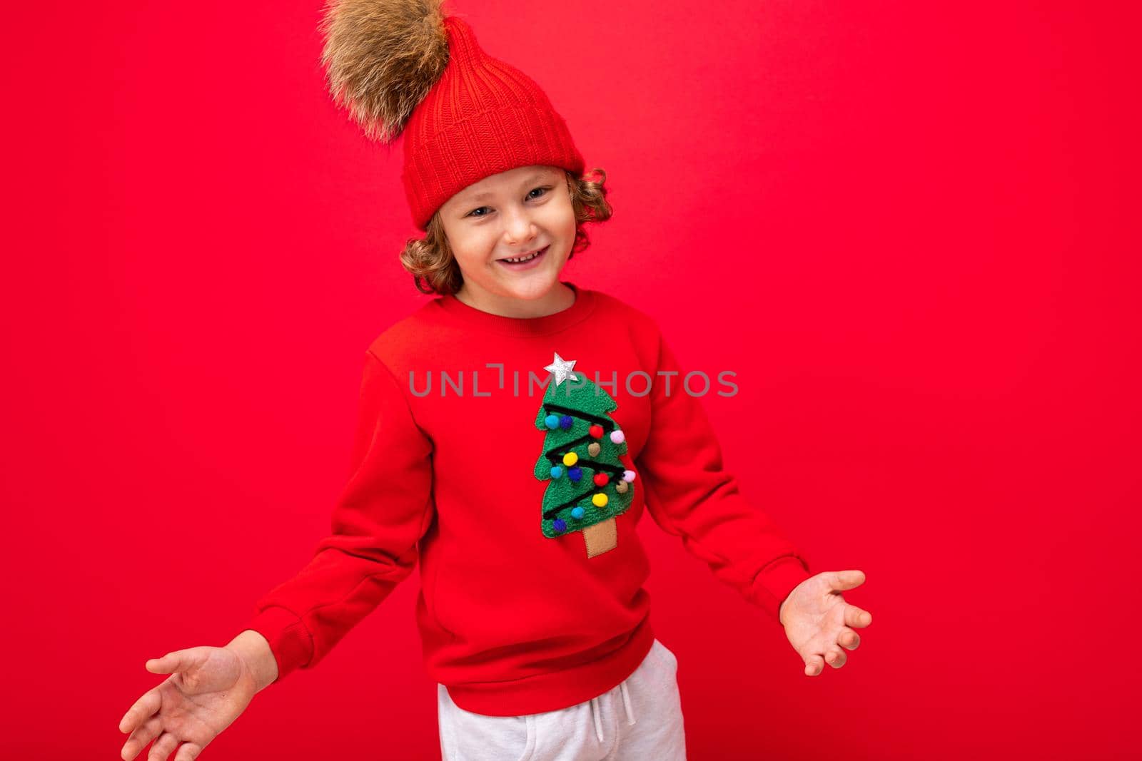 boy model on a red background, portrait of a cool blonde with curls in a sweater with a Christmas tree.