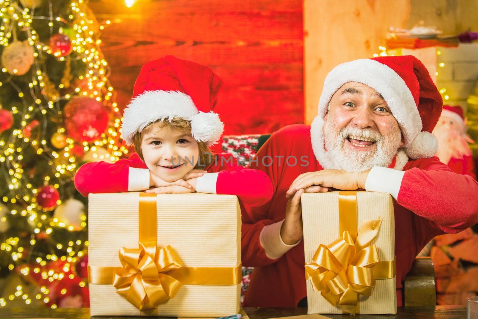 Child boy with grandfather Santa at home. Winter holidays. Santa boy celebrate christmas at home. Delivery christmas gifts. by Tverdokhlib