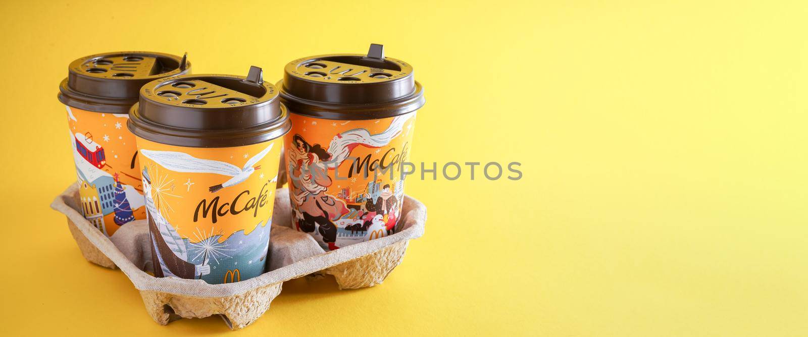 Ukraine, Kyiv - November 1, 2021: Yellow glass of coffee from McDonald's. Different winter paper glass drink McCafe. Coffee and cocoa cup on table with shadows. Menu in fastfood restaurant. by A_Gree