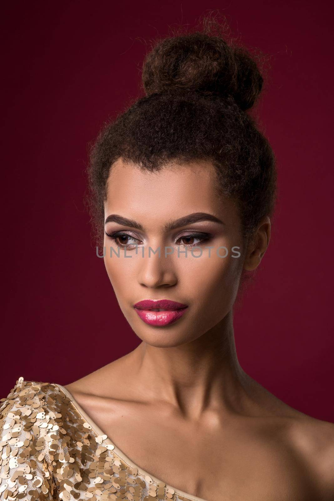 Fashion young African woman with make-up, in sexy gold dress. Model on a claret background in the studio