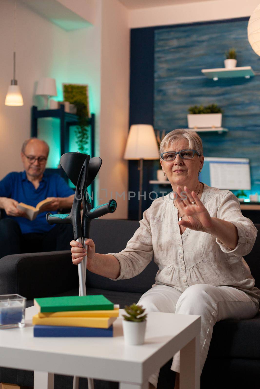 Retired woman with crutches waving on video call conference by DCStudio