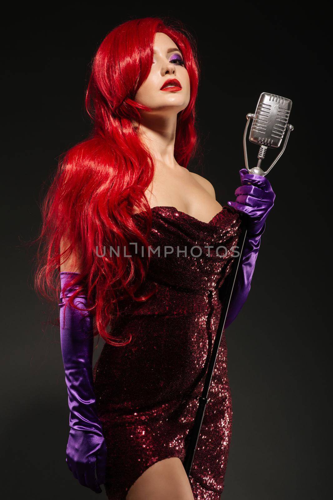 Young romantic redhead woman with very long hair in red gown with microphone on the stand on a black background. by zartarn