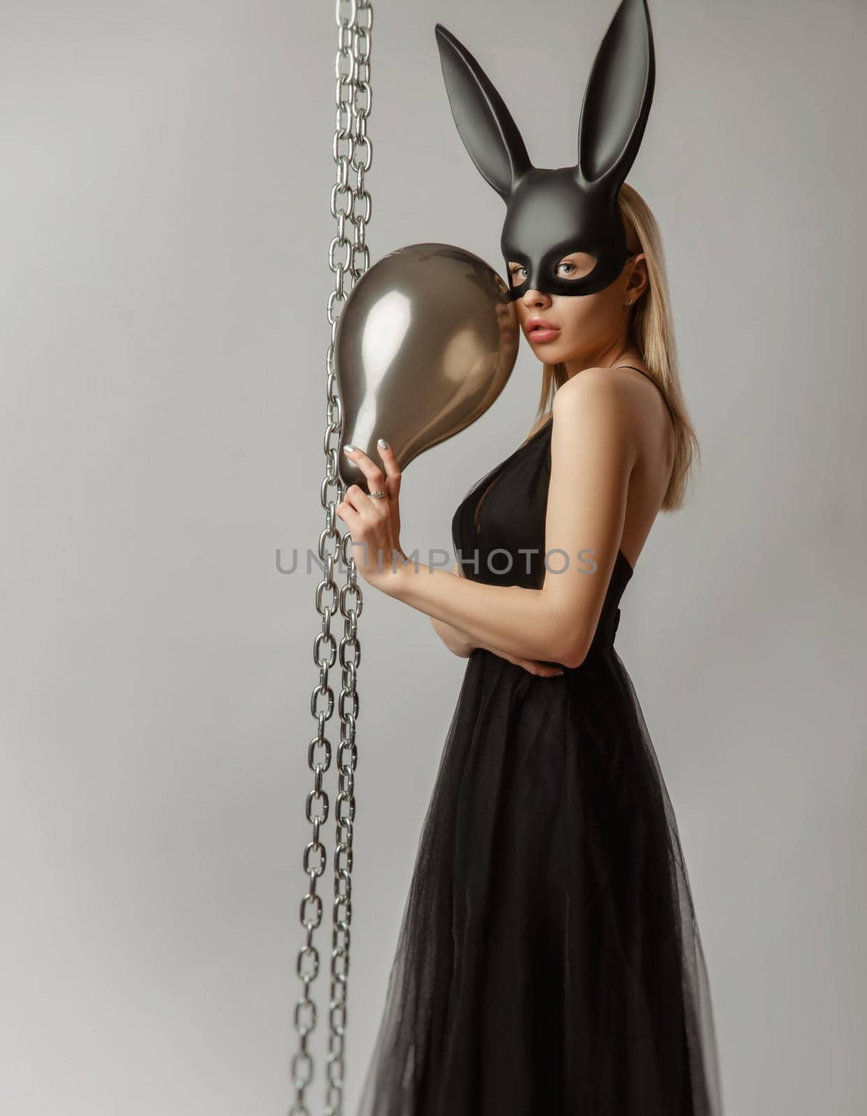 Beautiful blonde in a rabbit mask in a sexy evening dress on a white background with a metal chain by Rotozey