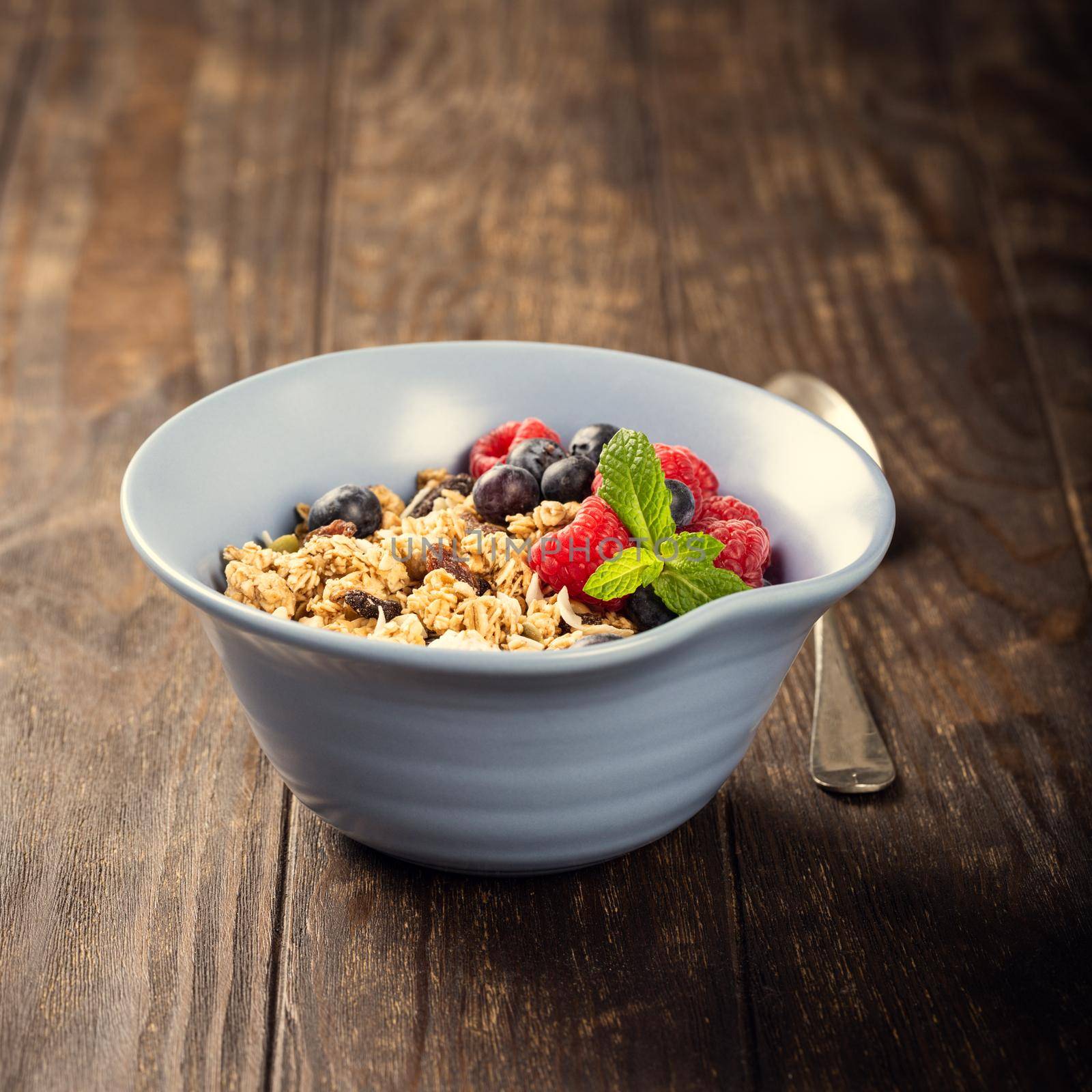 Oat granola with berries and yoghurt in blue bowl on dark old wooden background. Copy space. Healthy breakfast concept.