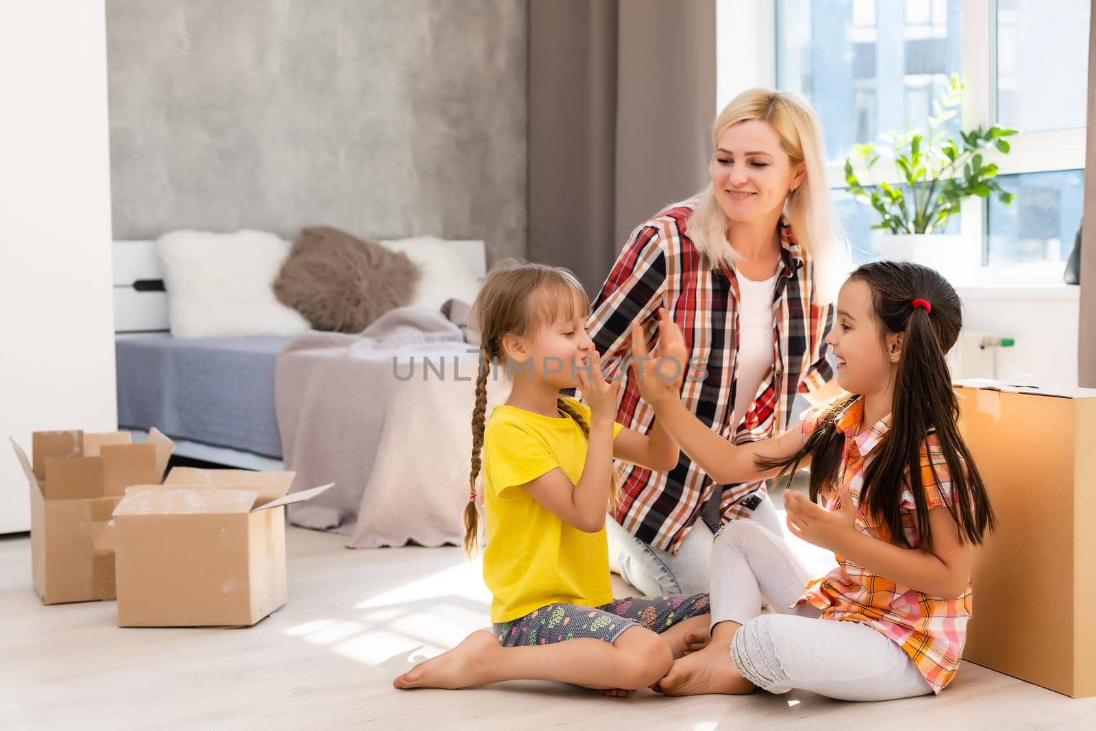 Happy family in living room. Preschool daughters sitting and help unpacking cardboard boxes belongings. Buy real estate, relocation at new modern house by Andelov13