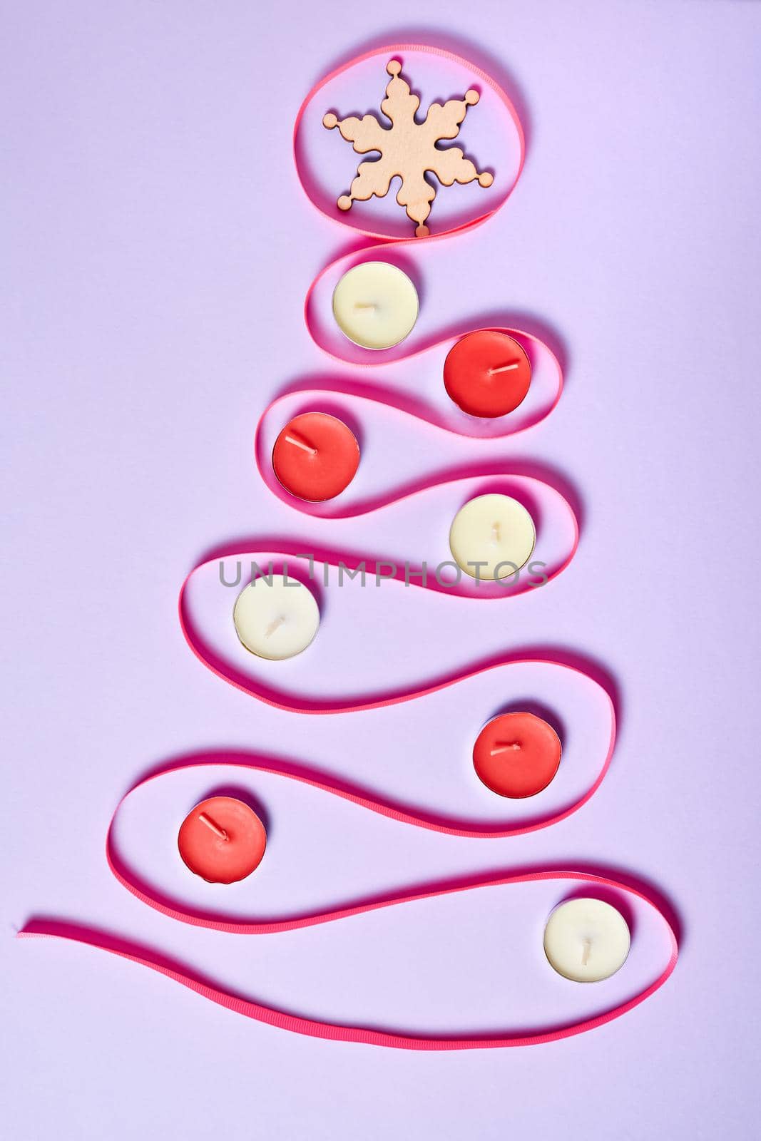 Christmas tree made of pink ribbon on purple paper background decorated with candles and Snowflake on the top of the tree