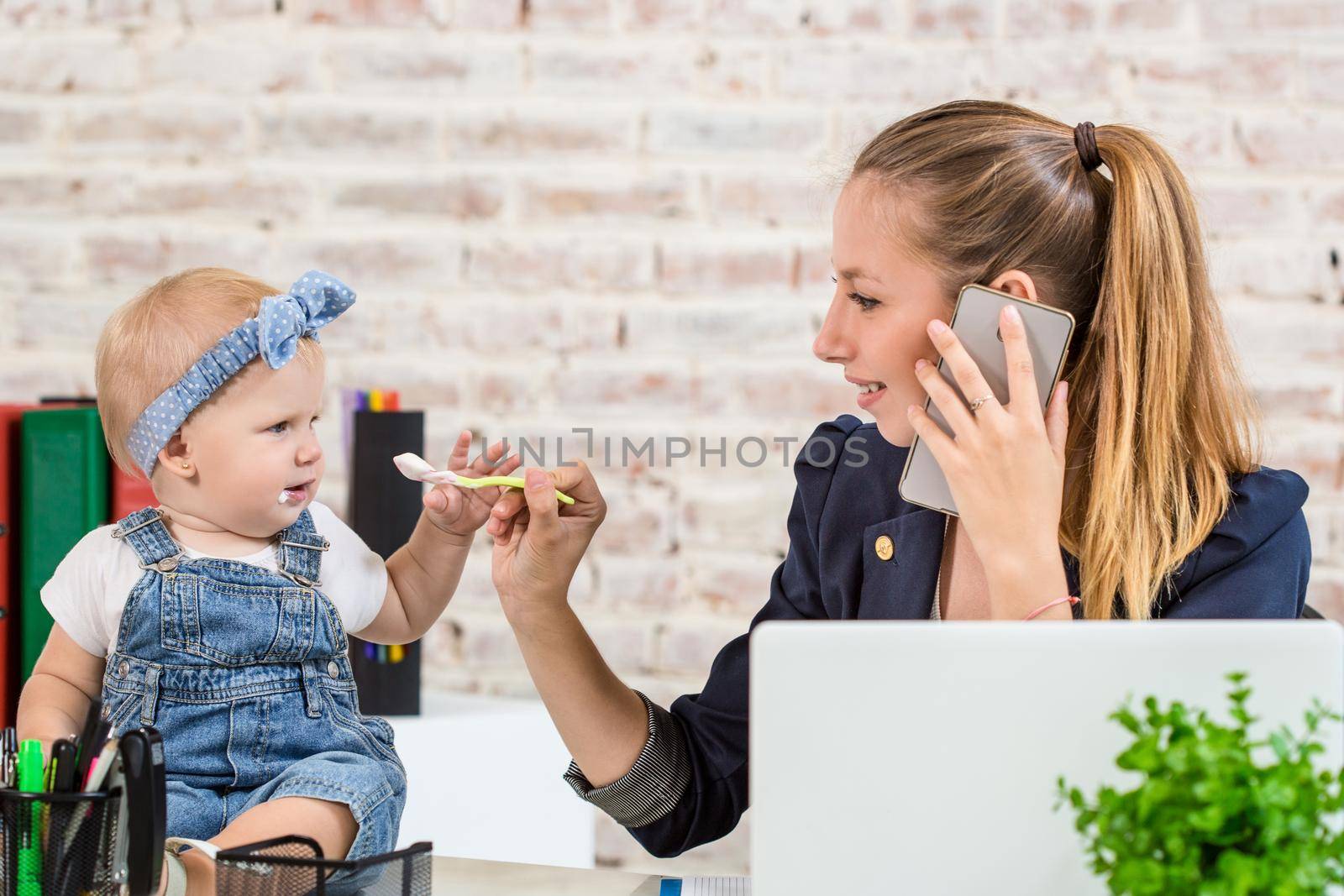 Family Business - telecommute Businesswoman and mother with kid is making a phone call. At the workplace, together with a small child