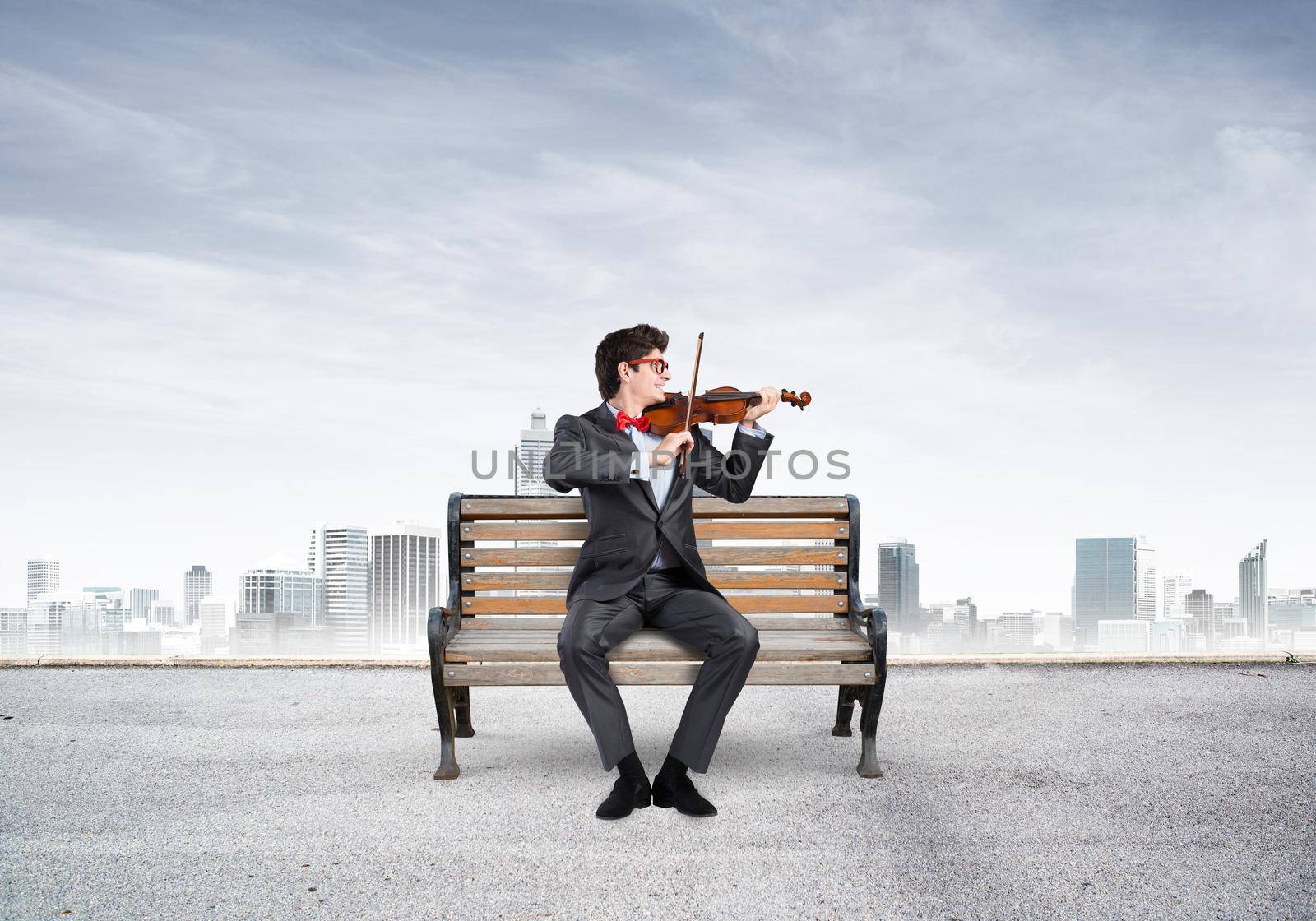 Young businessman plays the violin sitting on a wooden bench. Inspiration in business