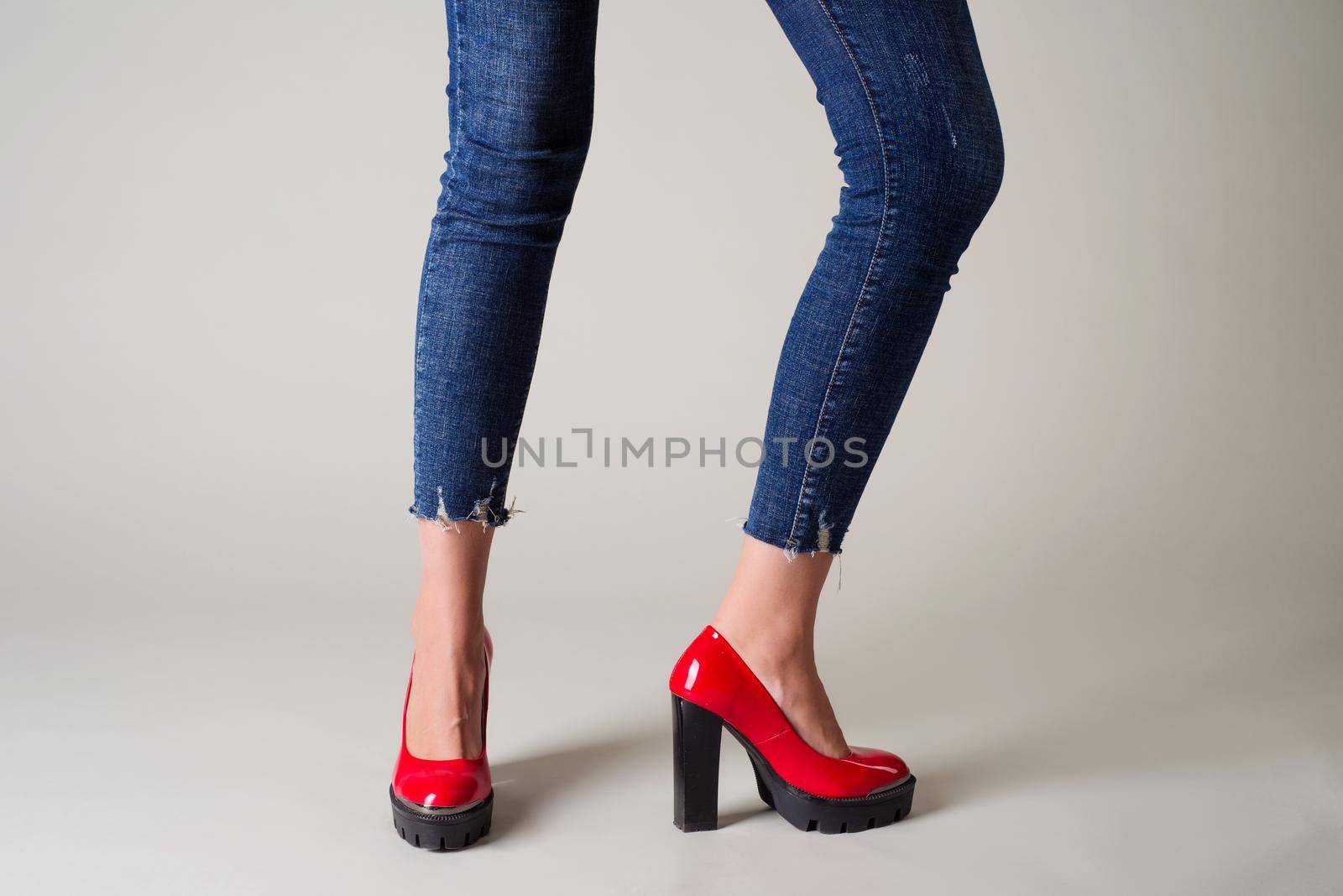 Woman in jeans red shoes with black heels posing on a gray background. - image