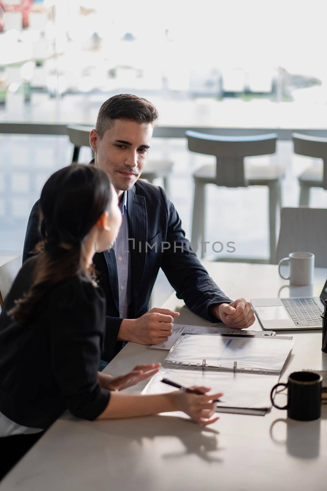 Multiethnic male caucasian mentor and female asian sitting at desk with laptop doing paperwork together discussing project financial report. Corporate business collaboration concept by nateemee