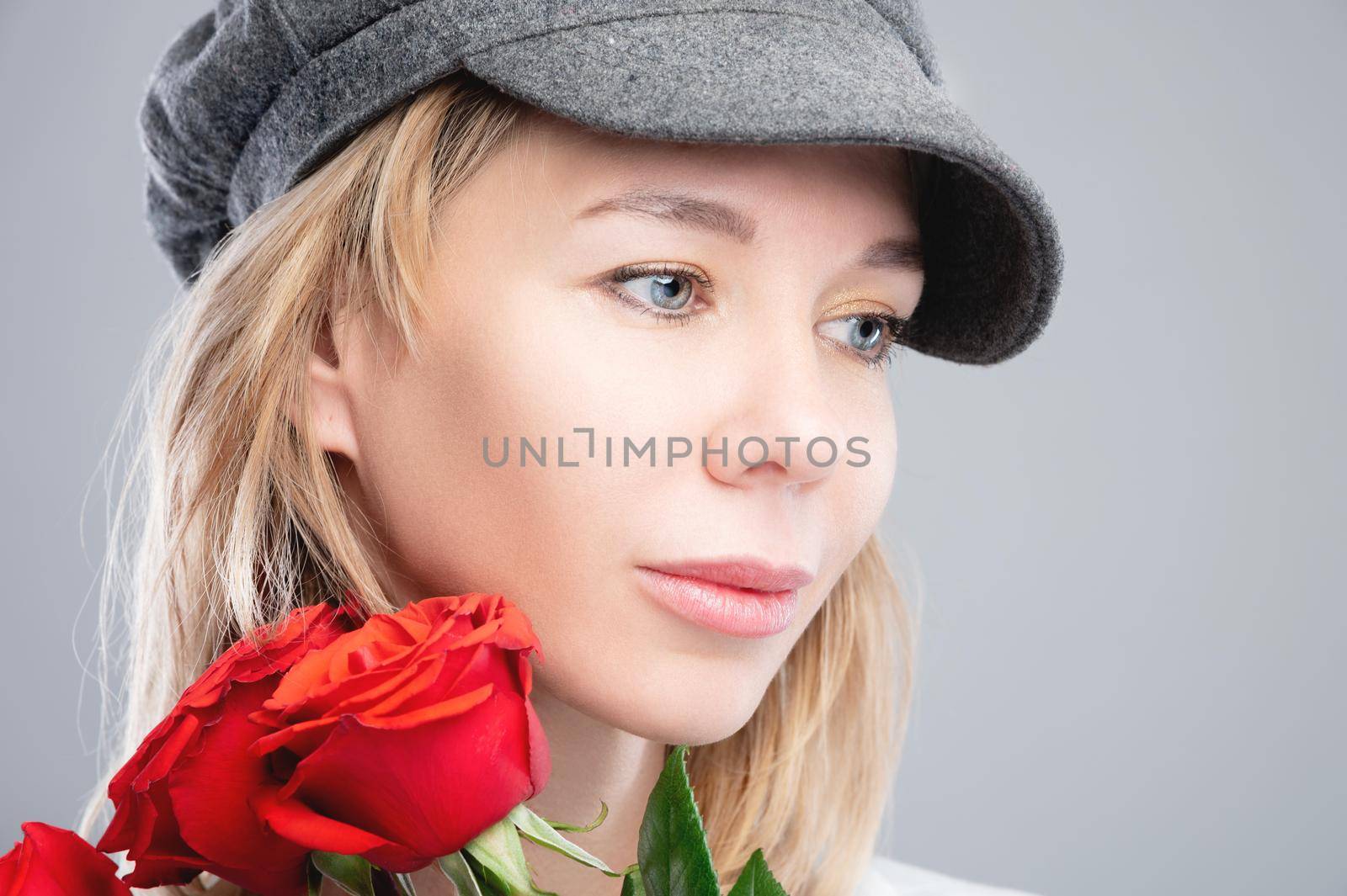 Close-up portrait of an attractive caucasian blonde girl in a retro cap with roses in her hands and looking to the side.