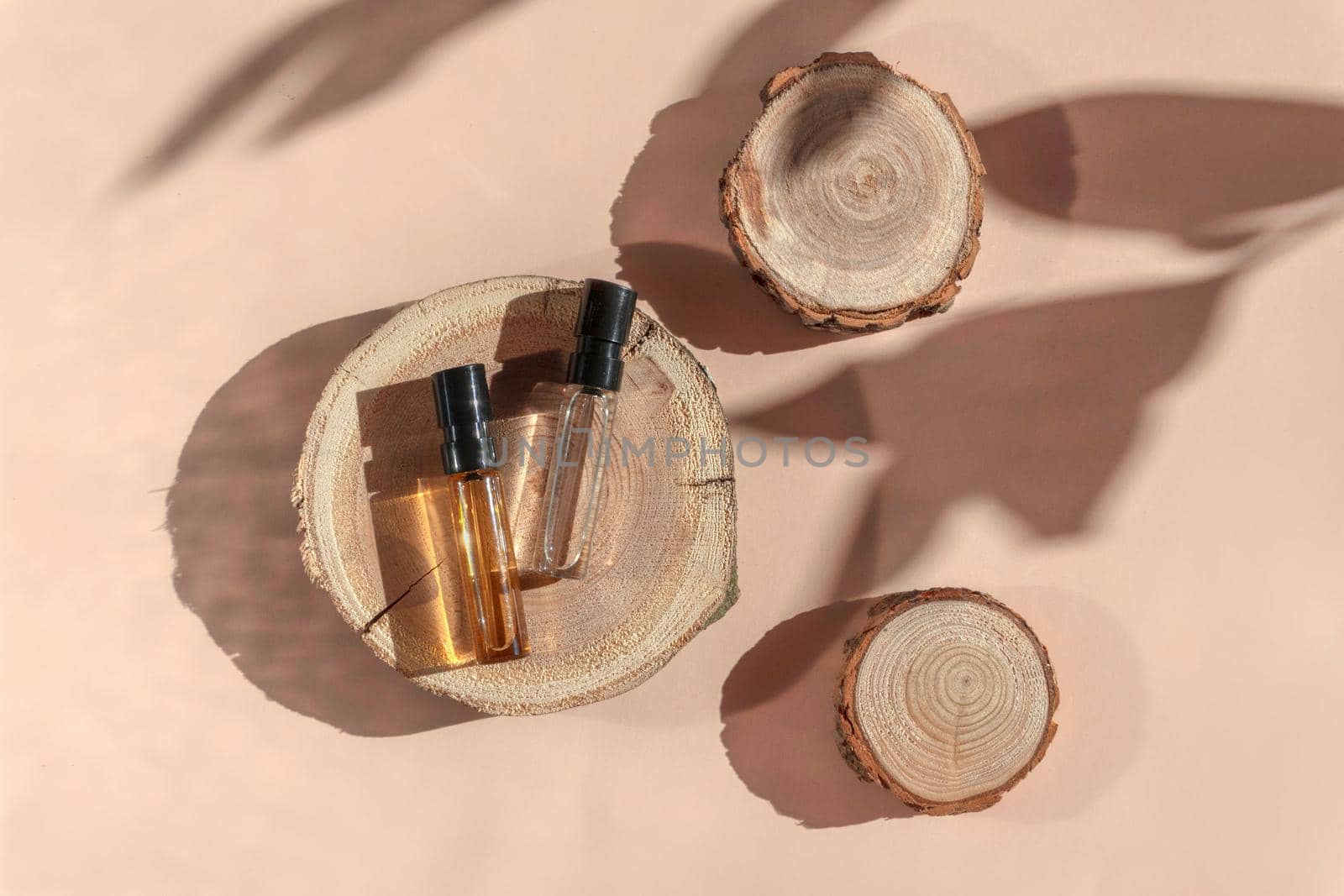 Perfume samples with yellow and transparent liquid on woodcut lying on beige background with shadows above. Luxury and natural cosmetic presentation. Testers in sunlight. Shades and lights. Top view