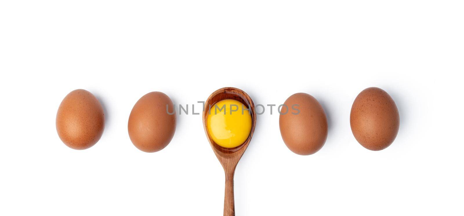 Brown eggs and egg yolk in wooden spoon on white background, top view