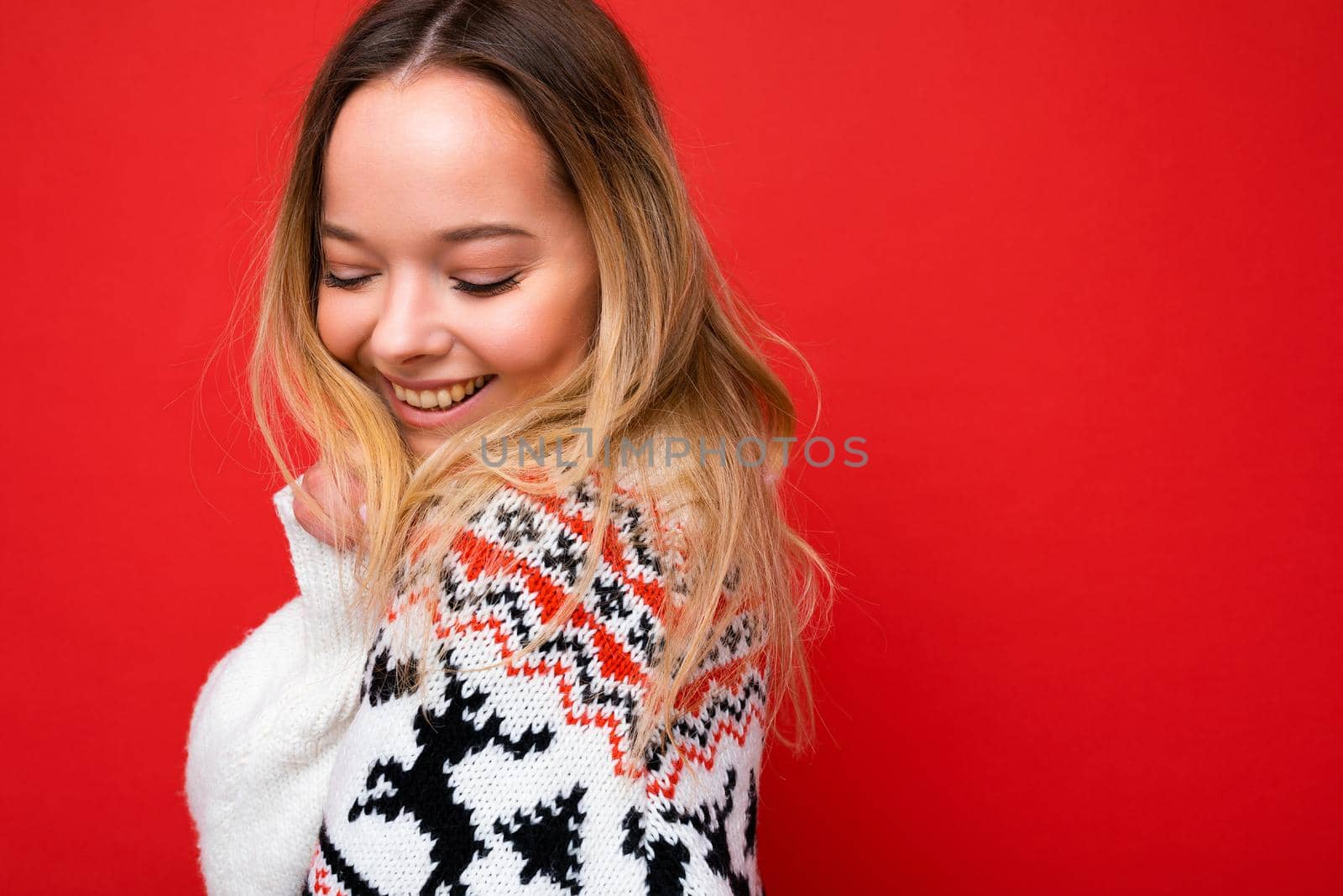 Photo shot of young beautiful cute happy blonde woman wearing winter sweater isolated over red background with copy space. Christmas concept.