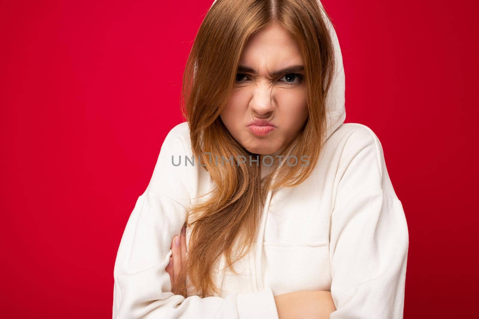 Dissatisfied angry young beautiful dark blonde female person with sincere emotions isolated on background wall with copy space wearing casual white hoodie. Negative concept.