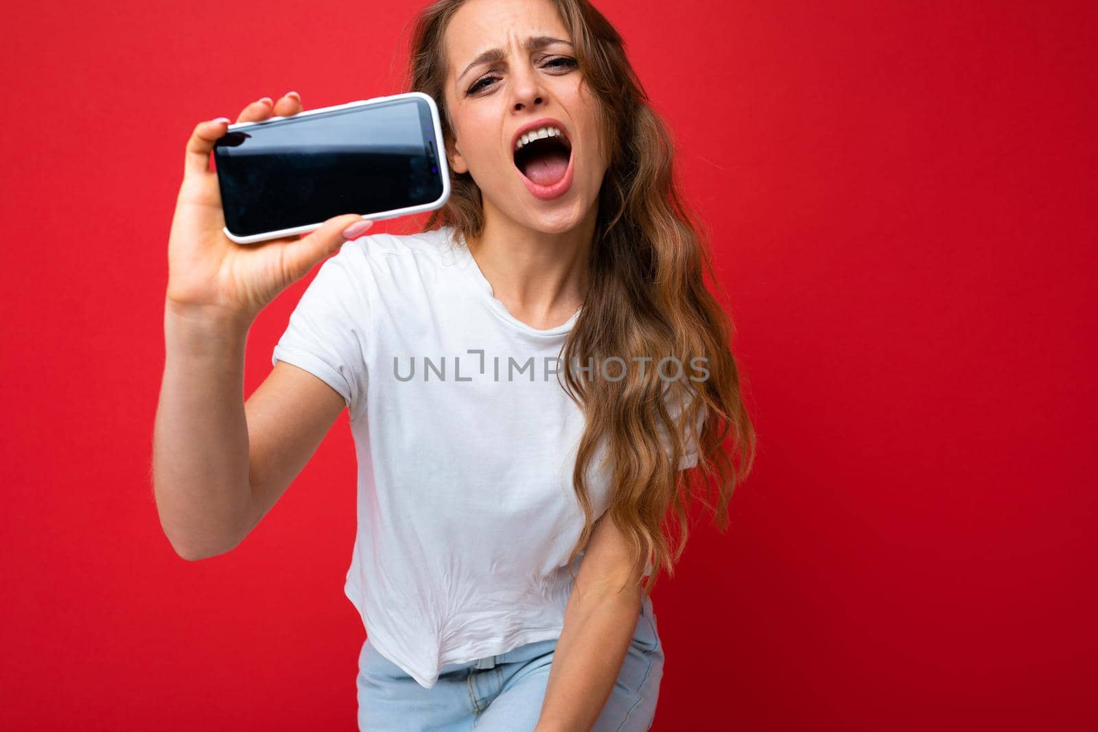 Image of a shocked young beautiful woman posing isolated over red wall background play games by mobile phone