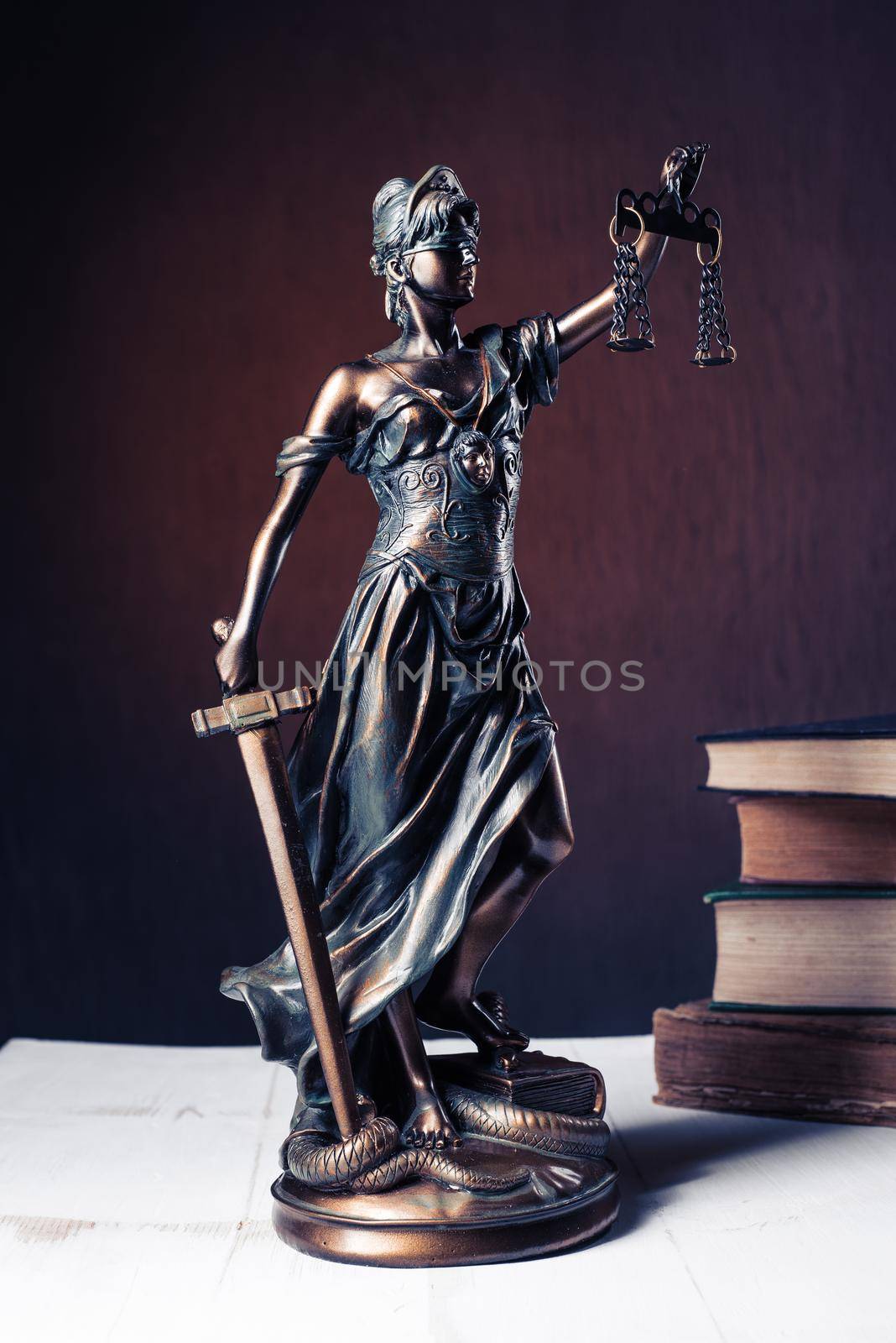 Themis figurine stands on a white wooden table next to a stack of old books. Scales Law Lawyer Business Concept. - Image