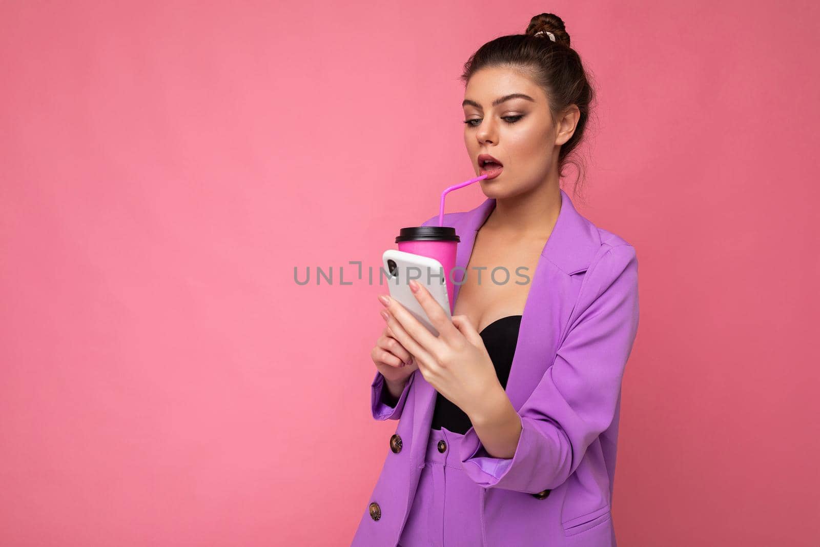 Young sexy positive woman isolated over pink background with copy space holding coffee to take away and a mobile phone.