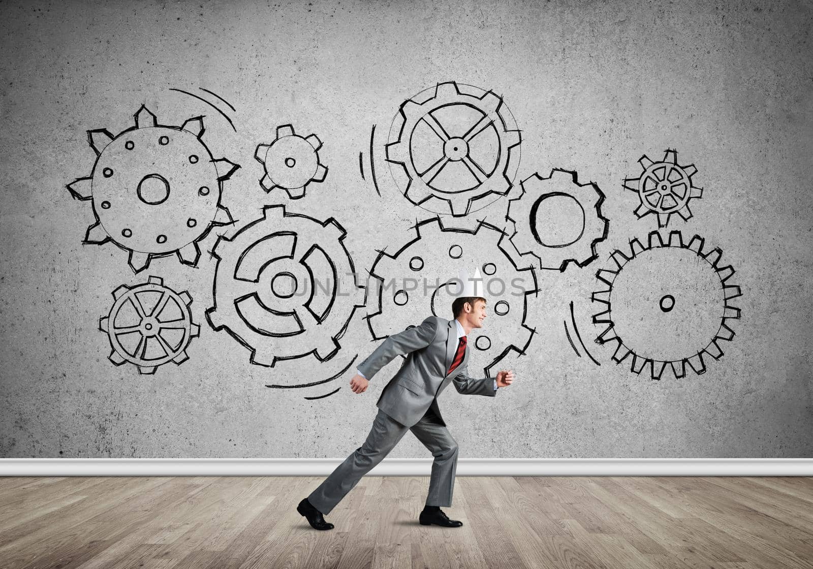 Young handsome businessman wearing white paper crown running and gear mechanism on wall