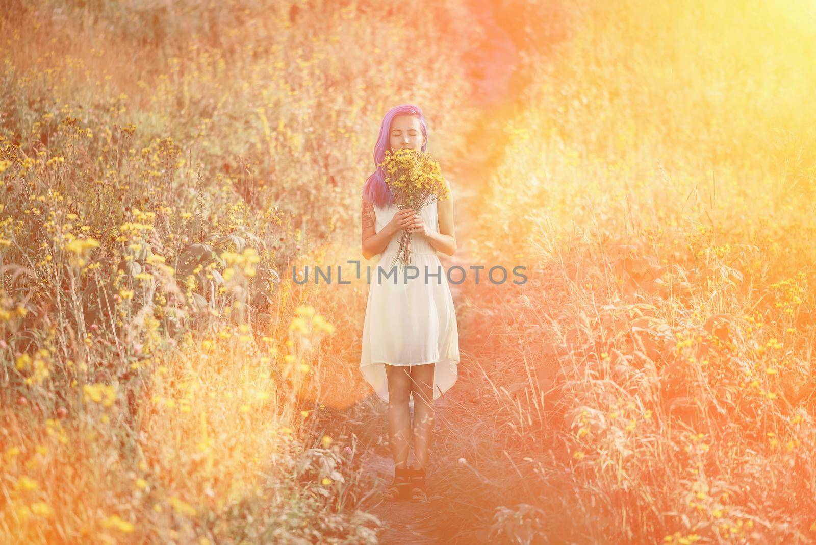 Young woman with blue hair and a bouquet of flowers standing in a field. Image with sunlight effect