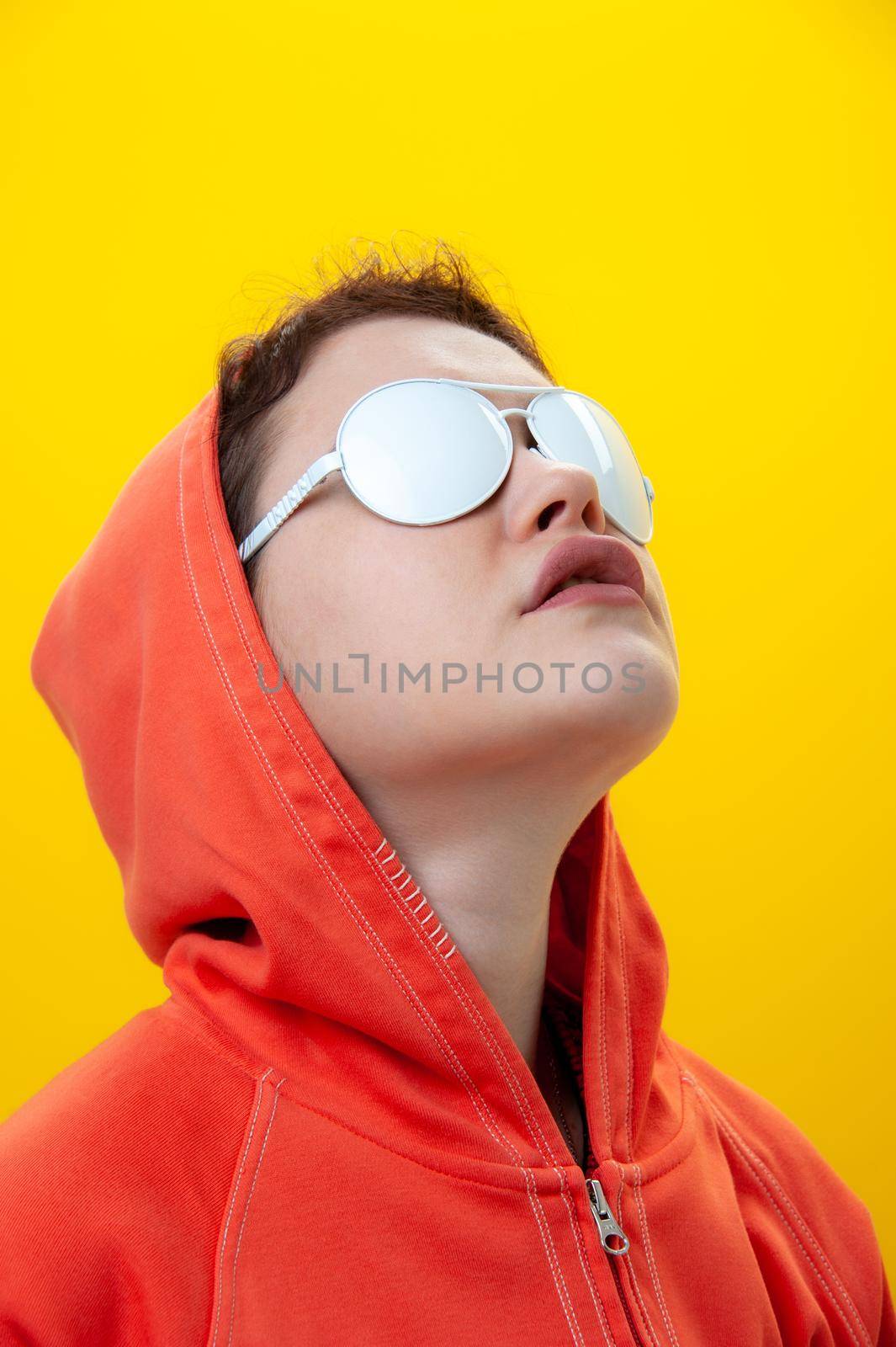 Alternative funky girl on a bright yellow background. Close up fashion portrait young beautiful woman in hoodie and white glasses. Unusual youth fashion concept. Hot image.