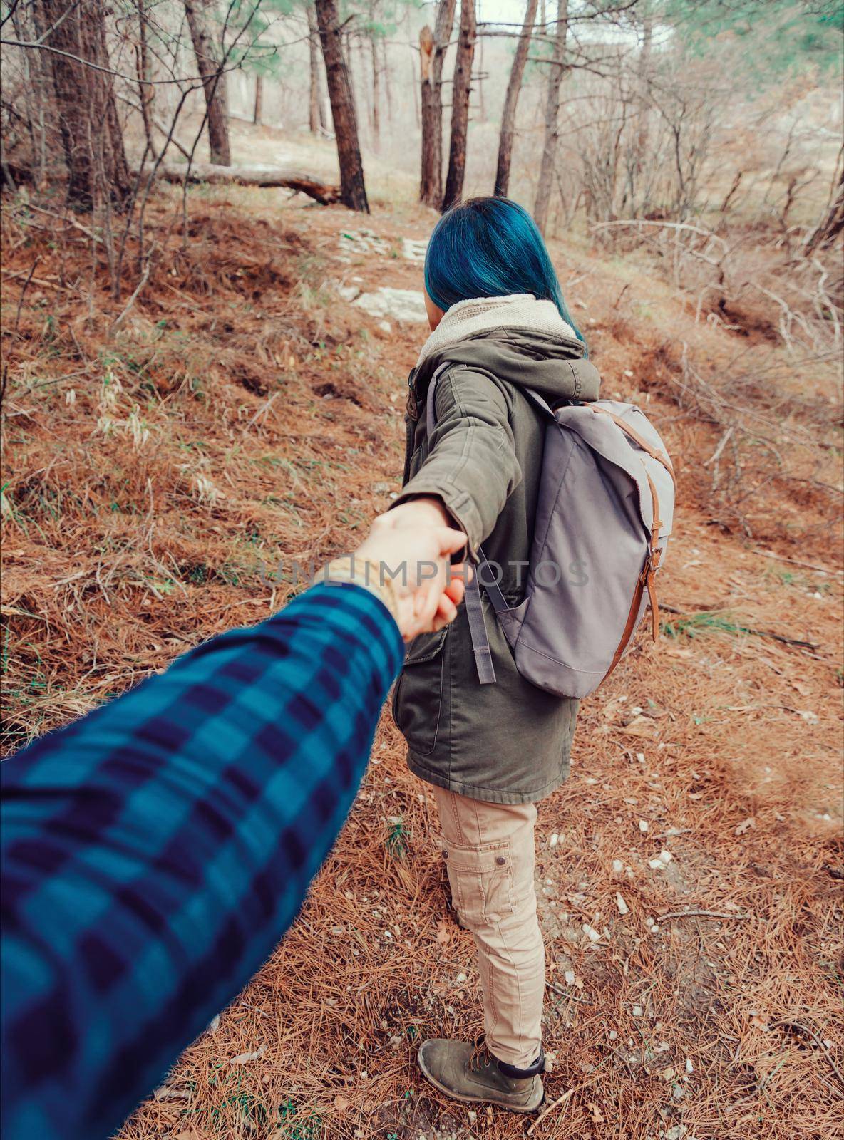 Hiker young woman with backpack holding man's hand and leading him in the forest outdoor. Point of view shot