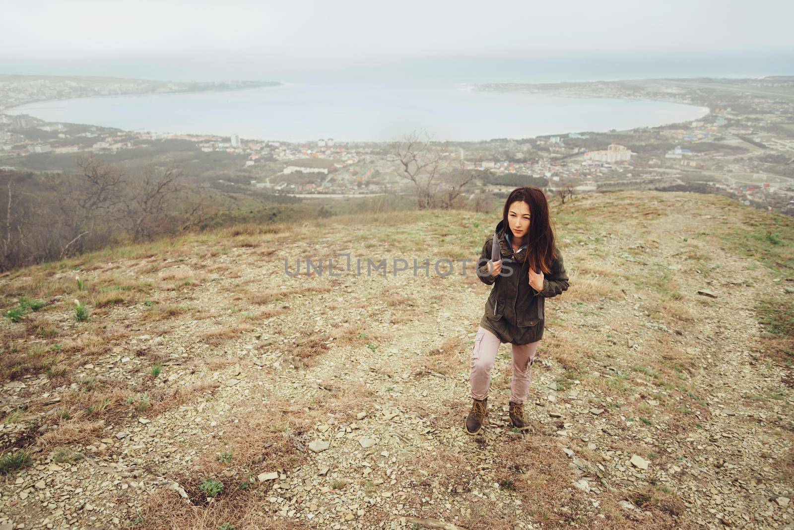 Hiker young woman with backpack walking up on mountain over the bay outdoor
