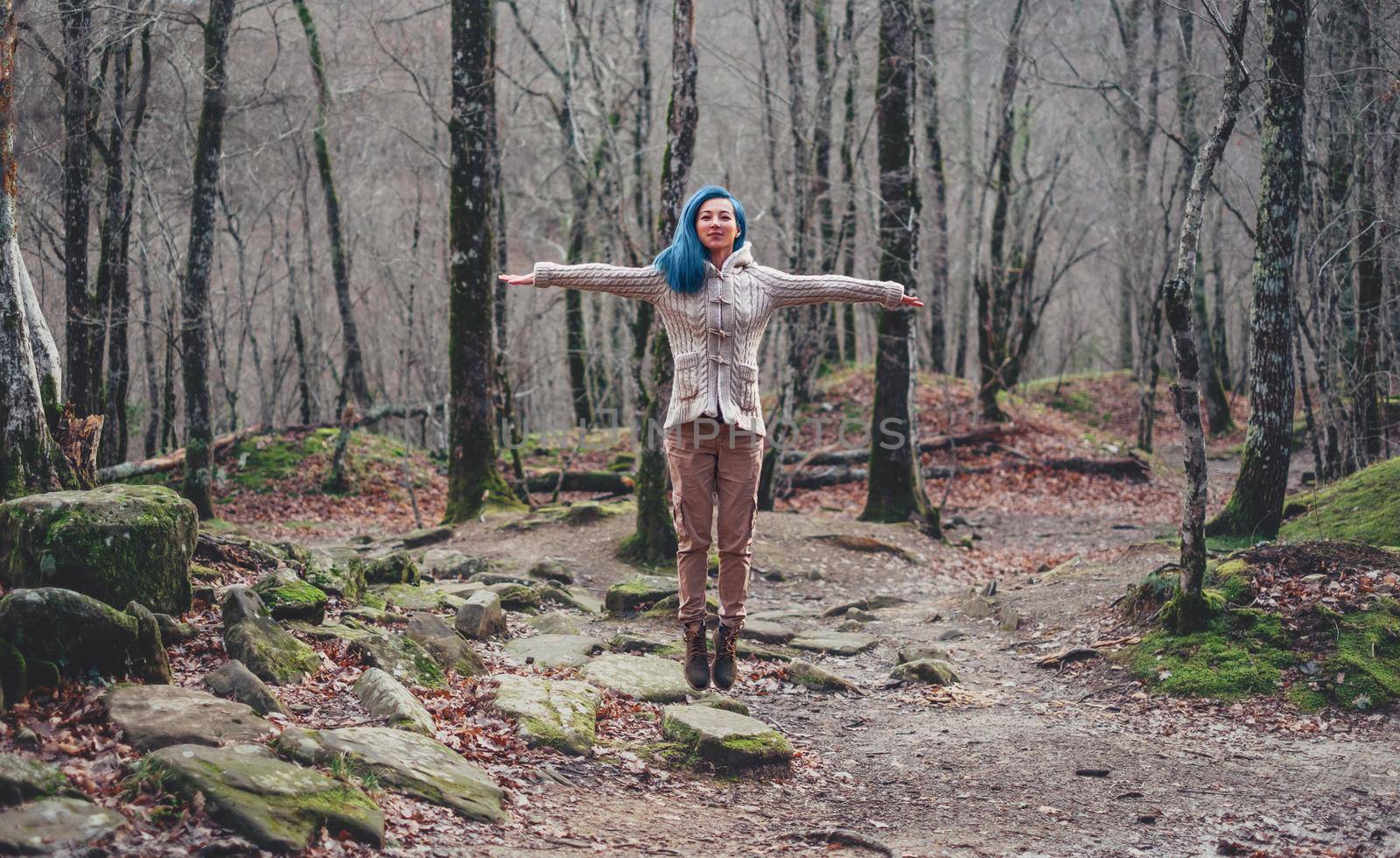 Happy young woman with blue hair jumping in autumn forest