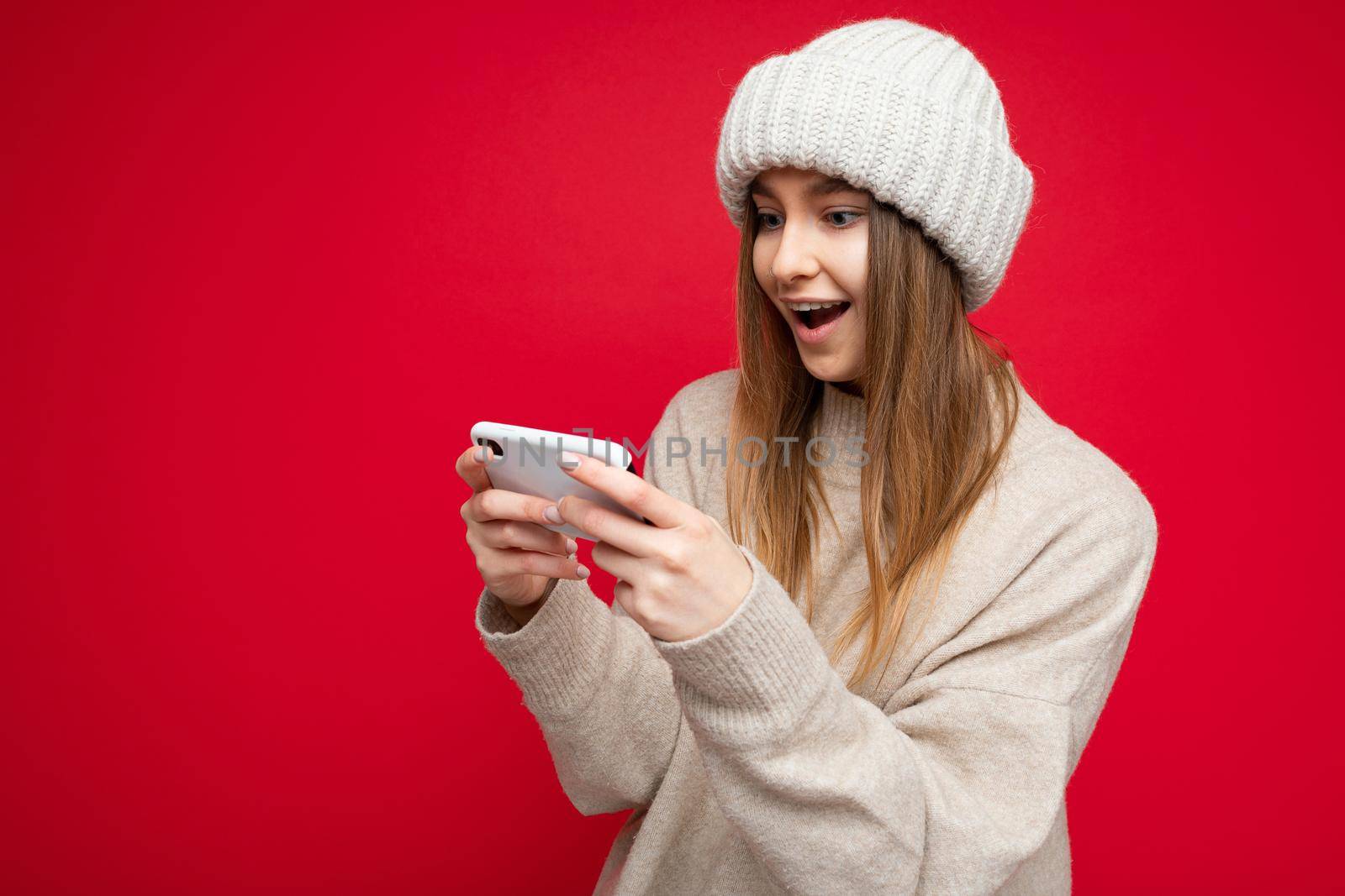Image of a shocked young beautiful woman posing isolated over red wall background play games by mobile phone. by TRMK