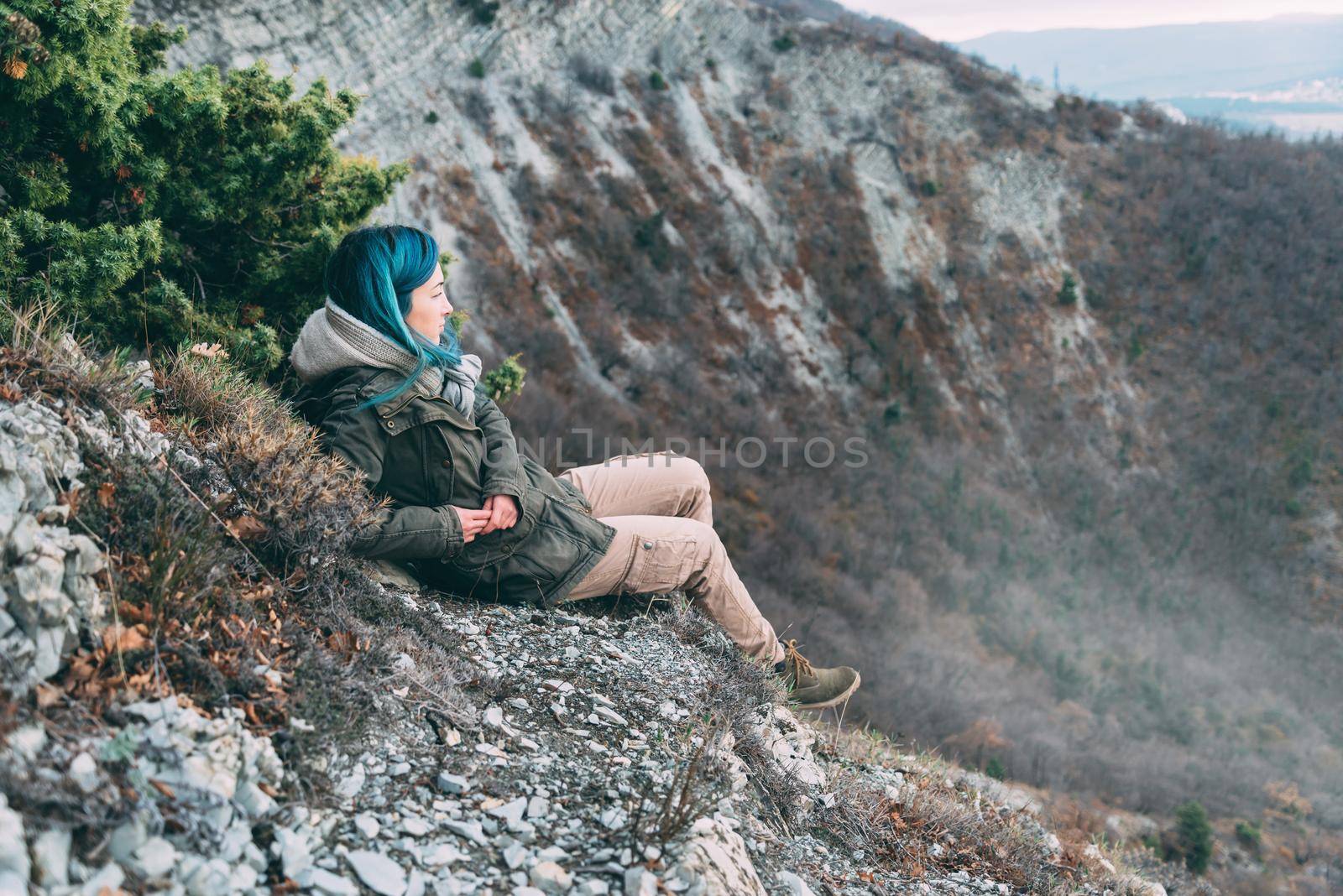 Young woman wearing parka jacket and cargo pants resting in the mountains and looking into the distance