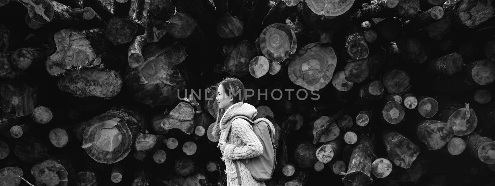 Hiker young woman with backpack walking on background of tree trunk. Black and white image