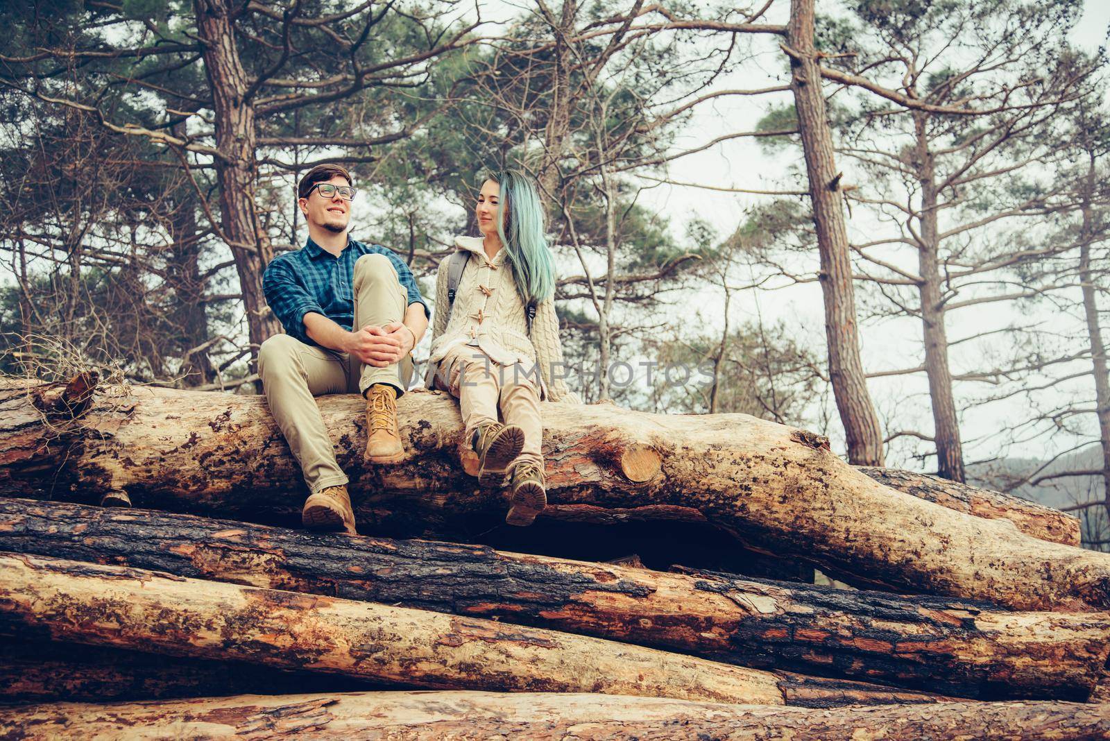 Loving couple sitting on fallen tree trunk in the forest. Traveler couple resting outdoor
