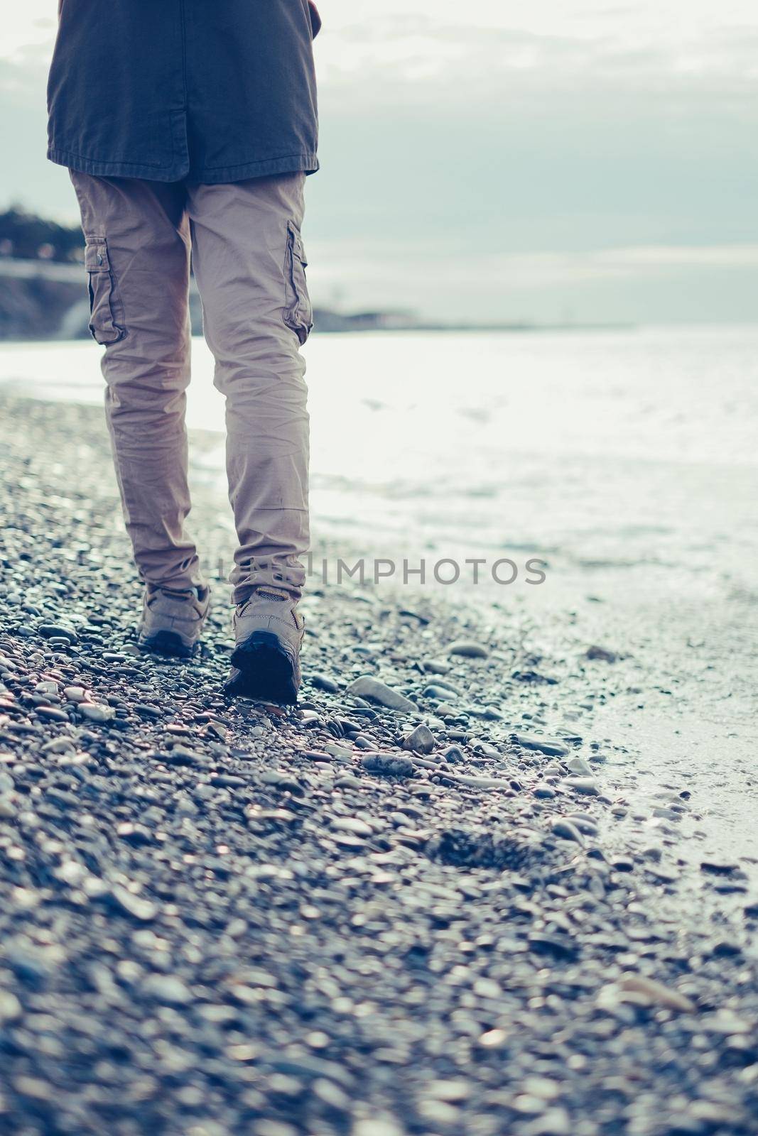 Traveler young woman walking on pebble coast near the sea, view of legs
