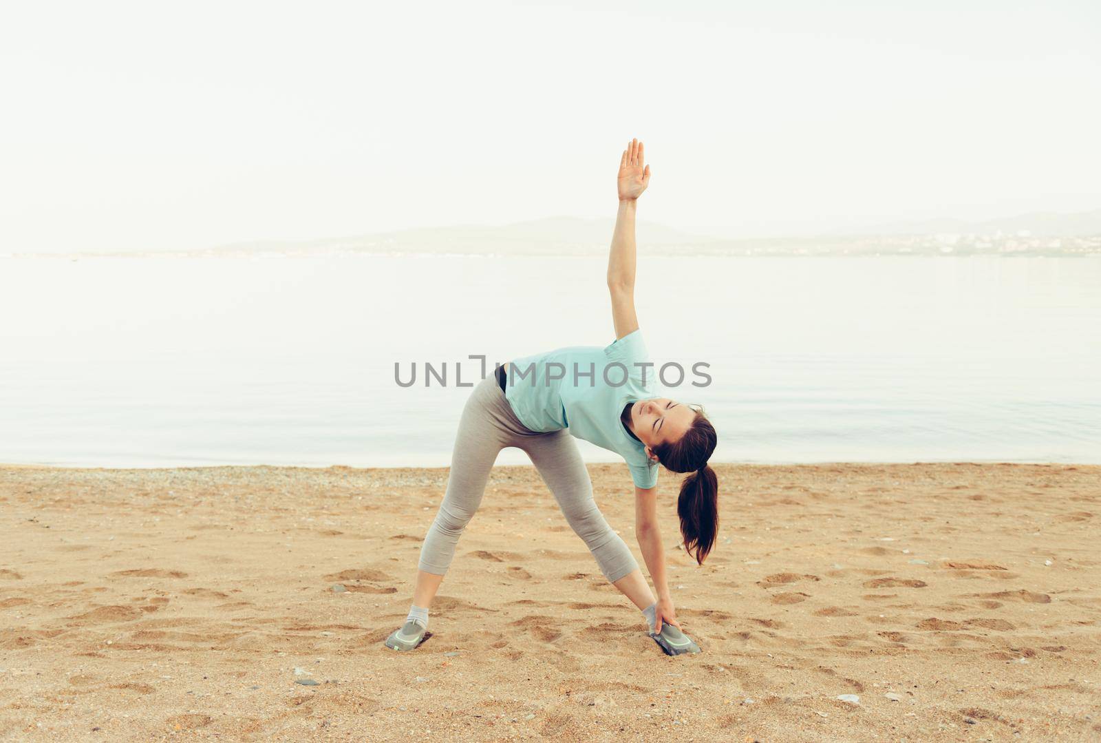 Sporty young woman stretching on sand beach in summer, workout. Concept of healthy lifestyle