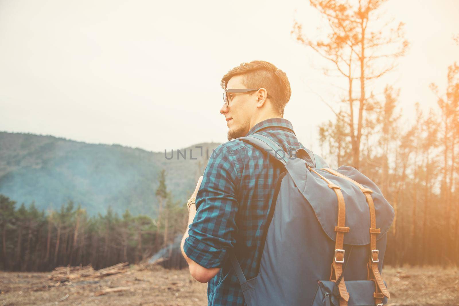 Handsome traveler young man with backpack walking in the forest at sunny day