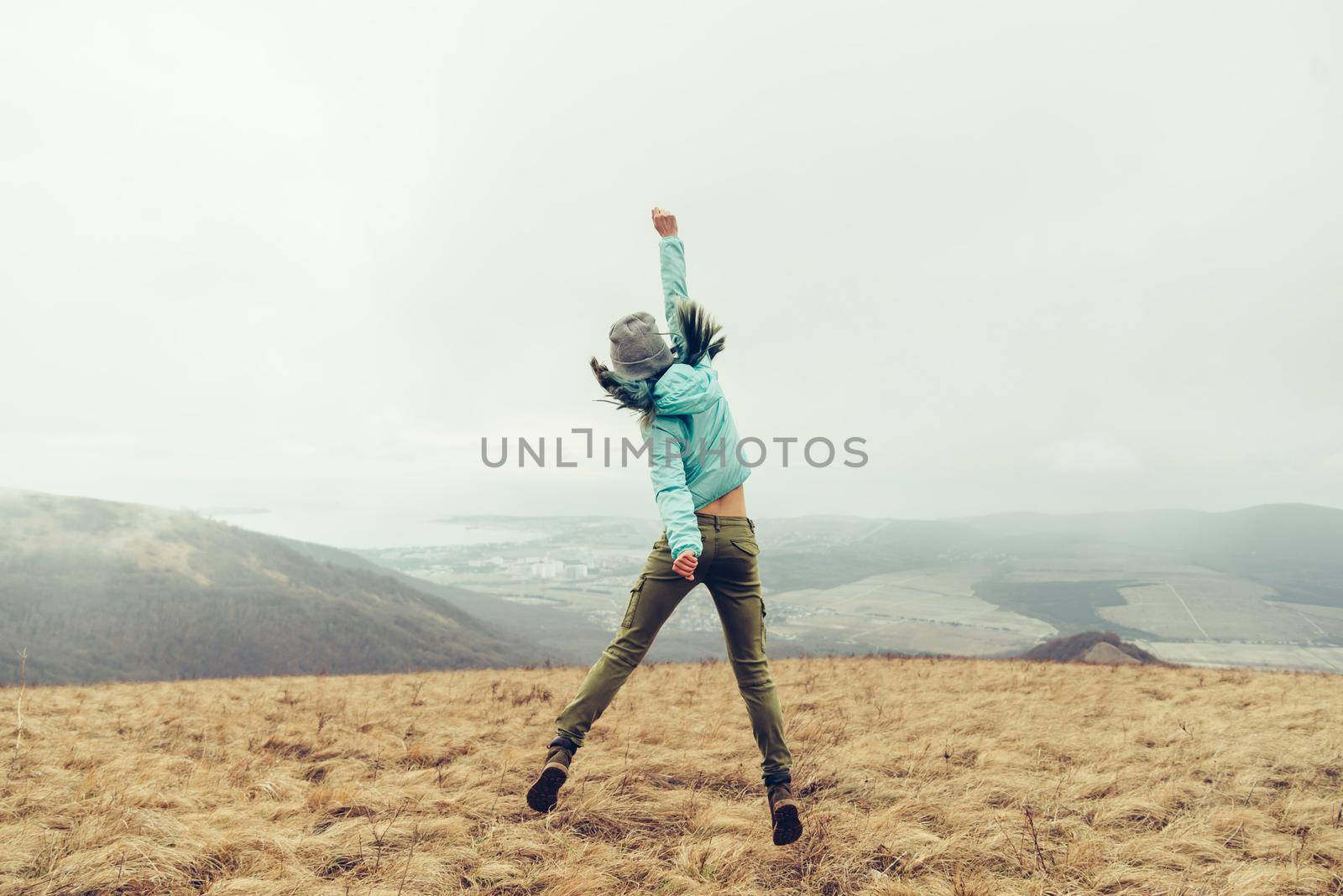 Unrecognizable happy young woman jumping on meadow in the mountains, rear view