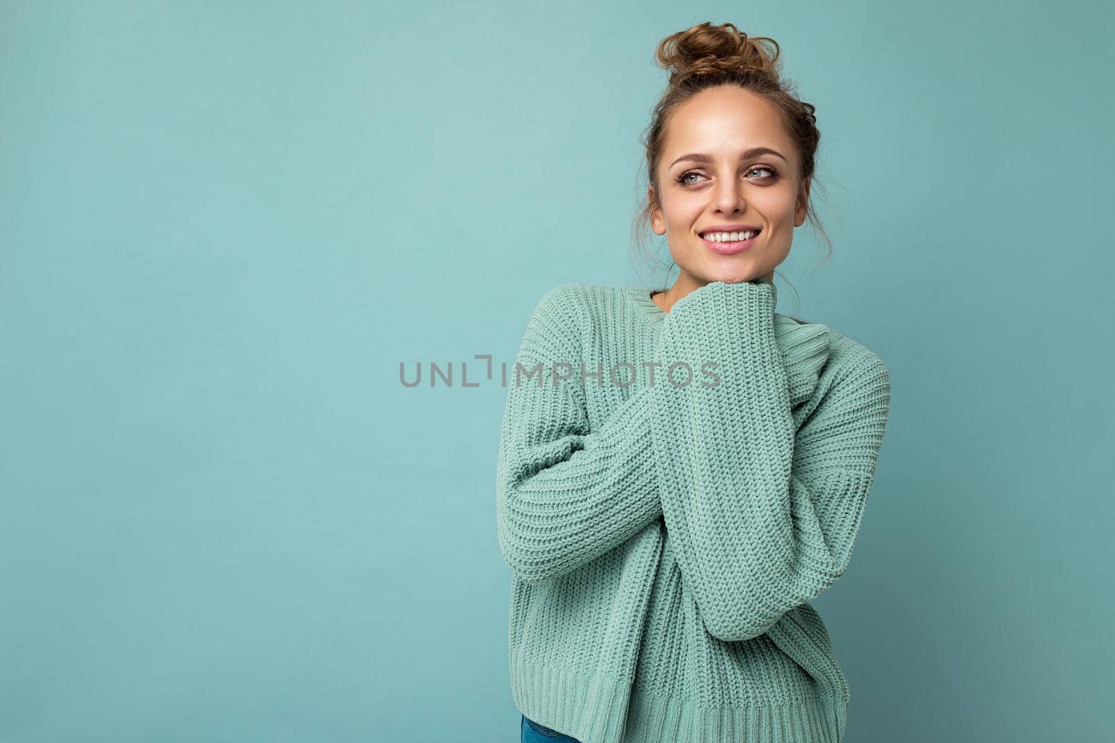 Young beautiful cute curly blonde woman with sexy expression, cheerful and happy face wearing trendy blue sweater isolated over blue background with copy space.