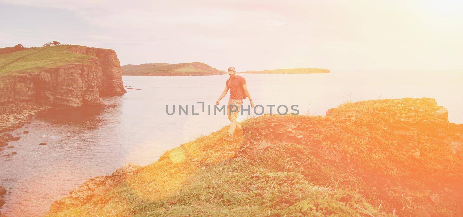 Hiker young man walking on coastline near the sea in summer. Image with sunlight effect