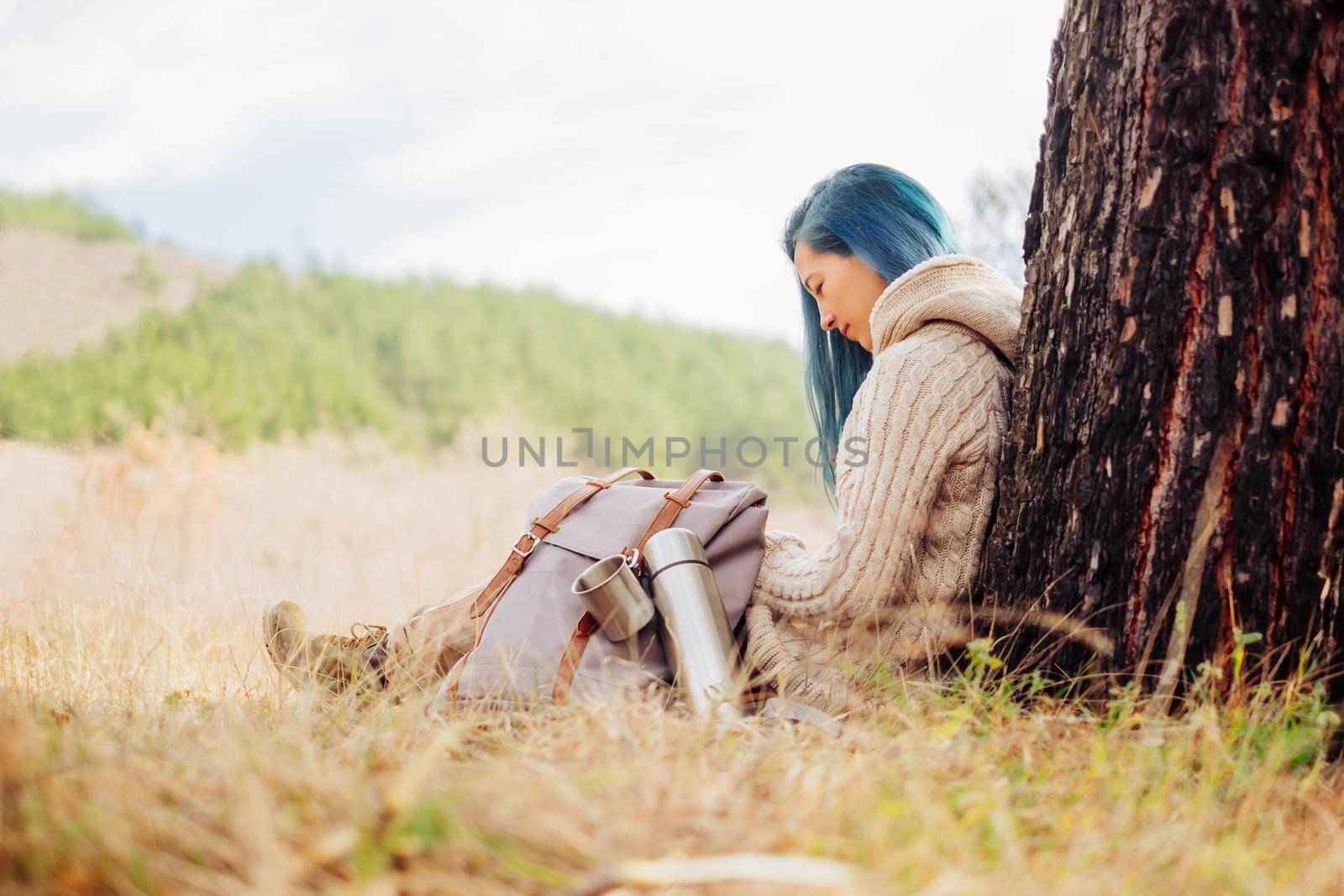 Traveler young woman with backpack and thermos sitting near the tree outdoor in spring