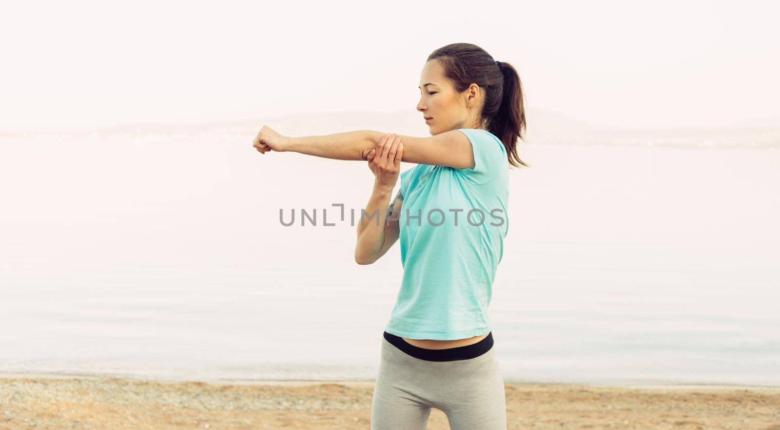 Sporty young woman stretching her arms on beach in summer in the morning, workout. Concept of healthy lifestyle