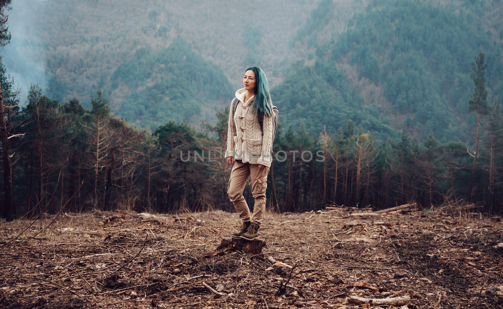 Traveler young woman with backpack standing on tree stump in the forest outdoor